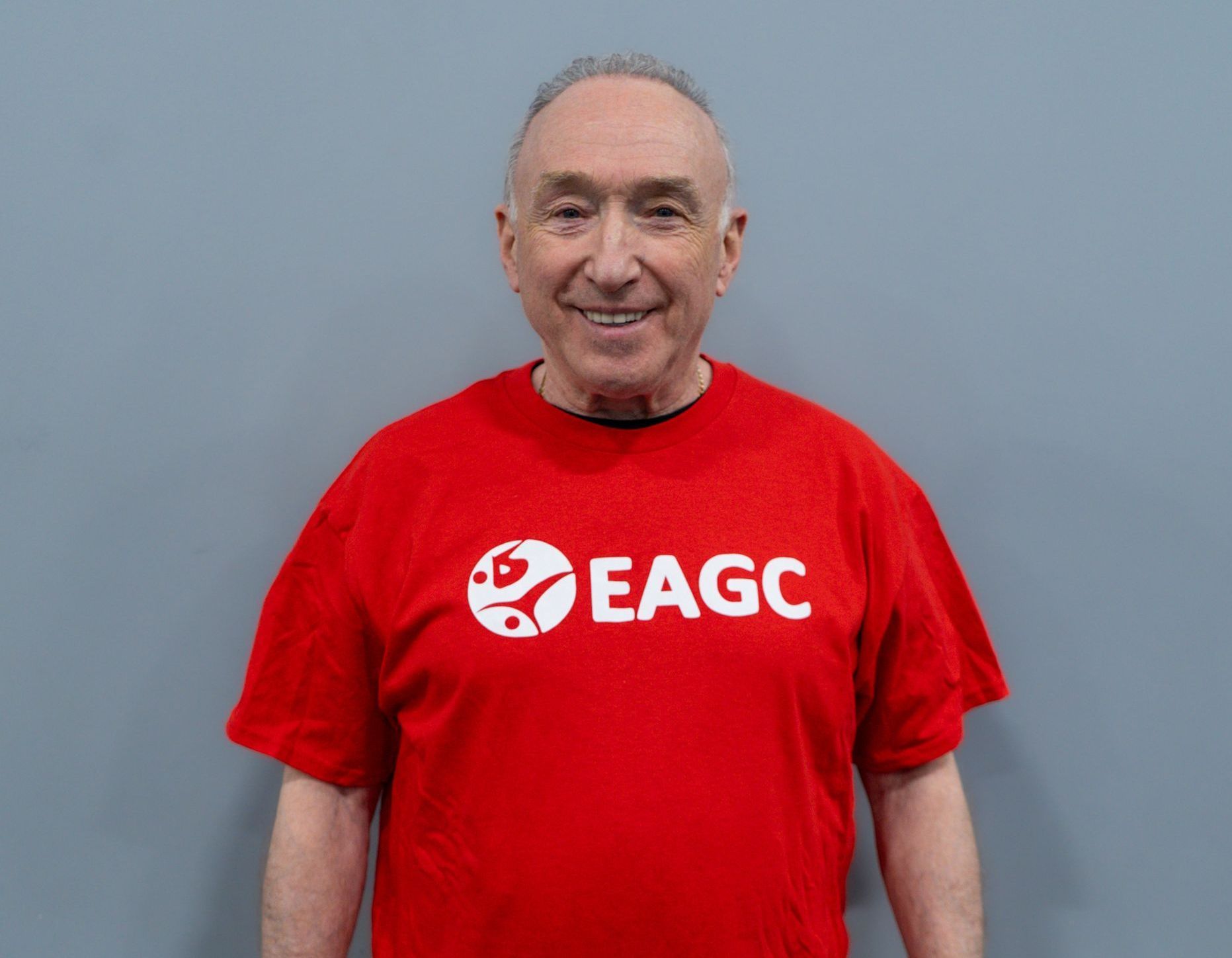 A man is wearing a red eagc t-shirt and smiling.