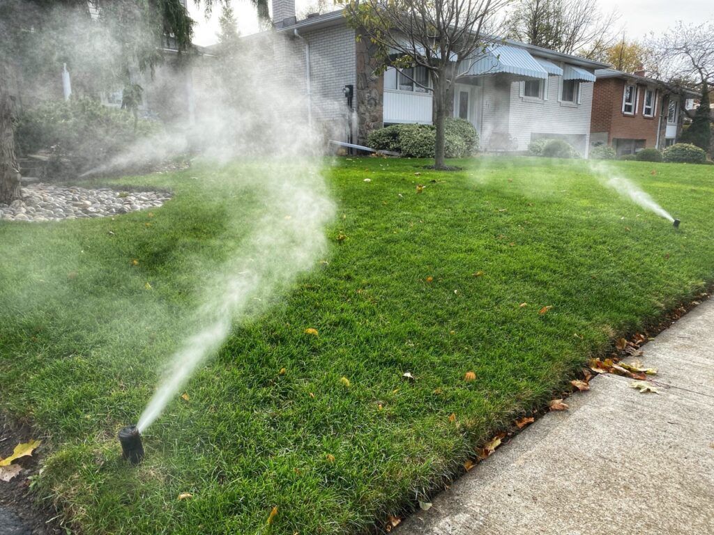 Sprinklers watering a green lawn beside a sidewalk in a residential yard