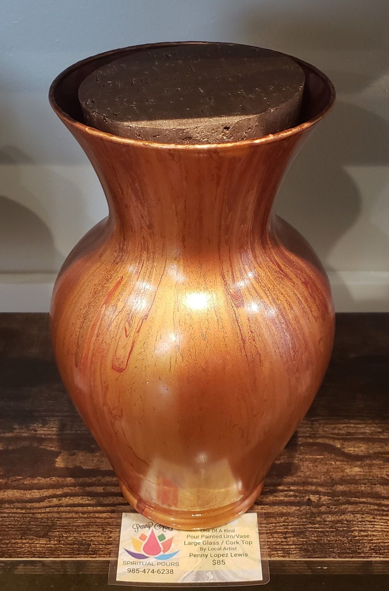 Bronze vase with dark top, set on a wooden surface, small label in front.
