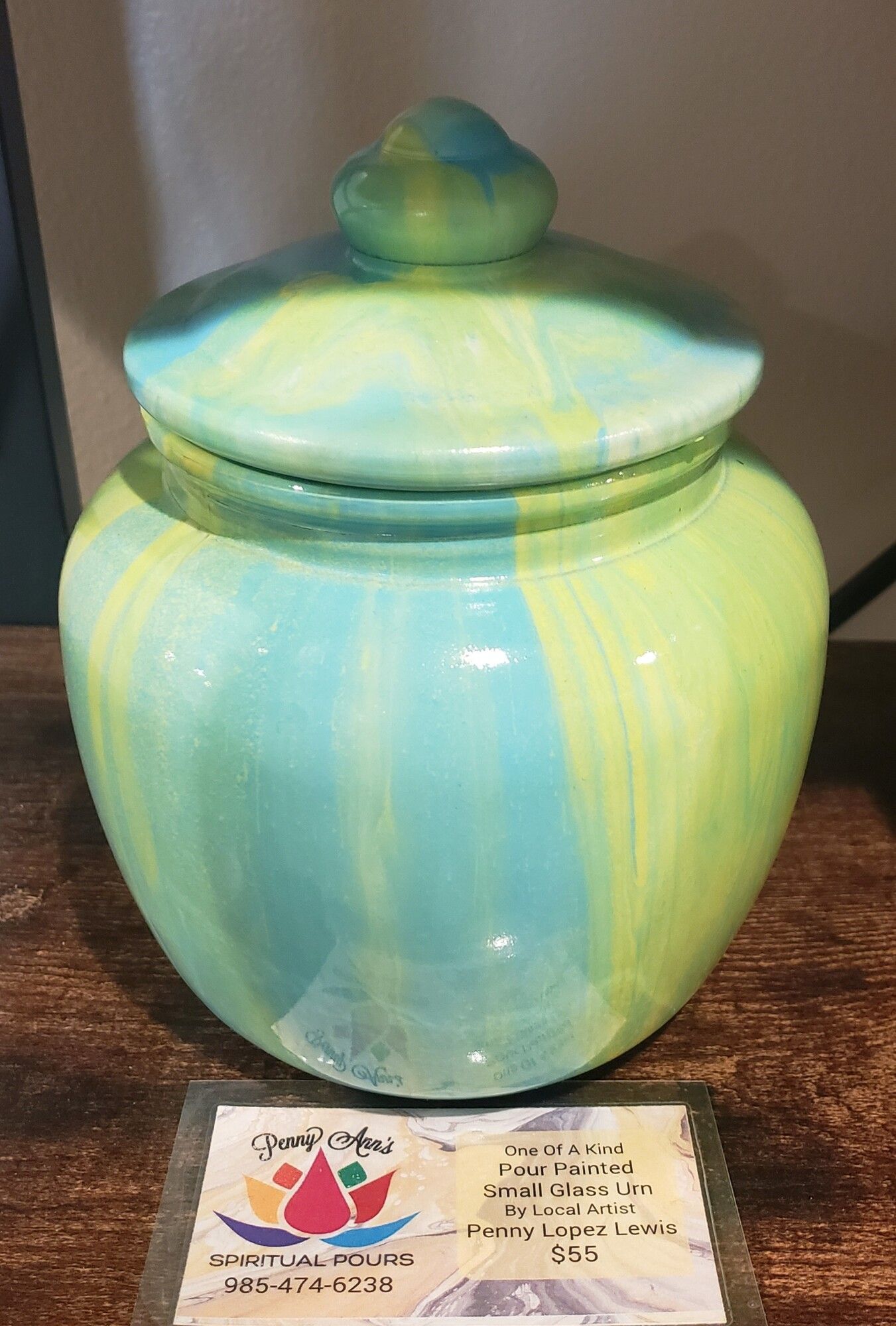 A round turquoise and yellow ceramic jar with a lid on a wooden surface.