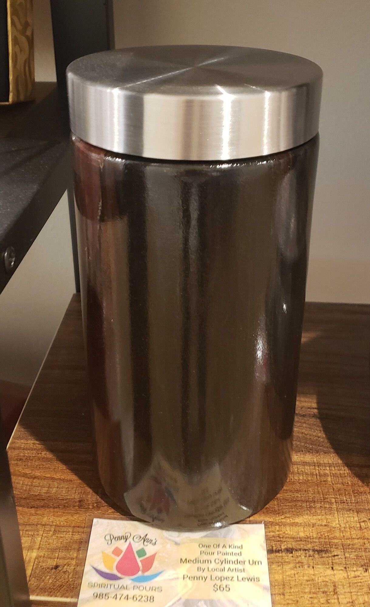 Dark jar with silver lid on a wooden shelf. A small label rests in front.