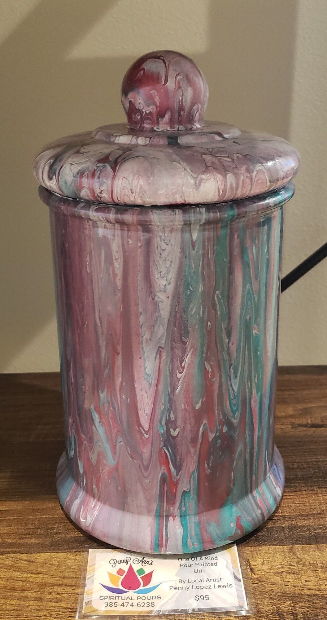 Purple, teal, and white paint-poured decorative jar with lid and top knob sitting on a wooden surface.