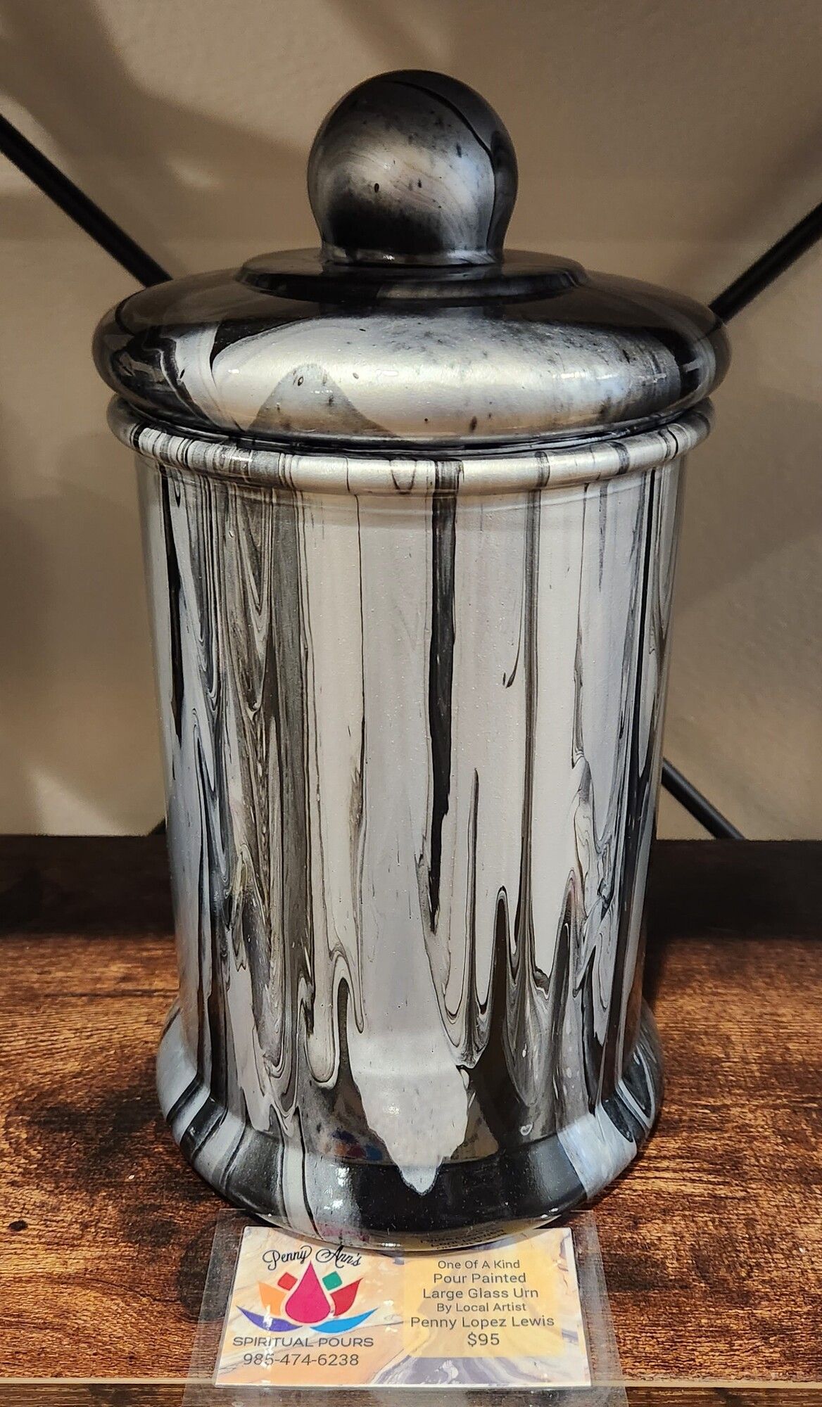 Silver and black dripped-paint jar with lid, set on a wooden surface.