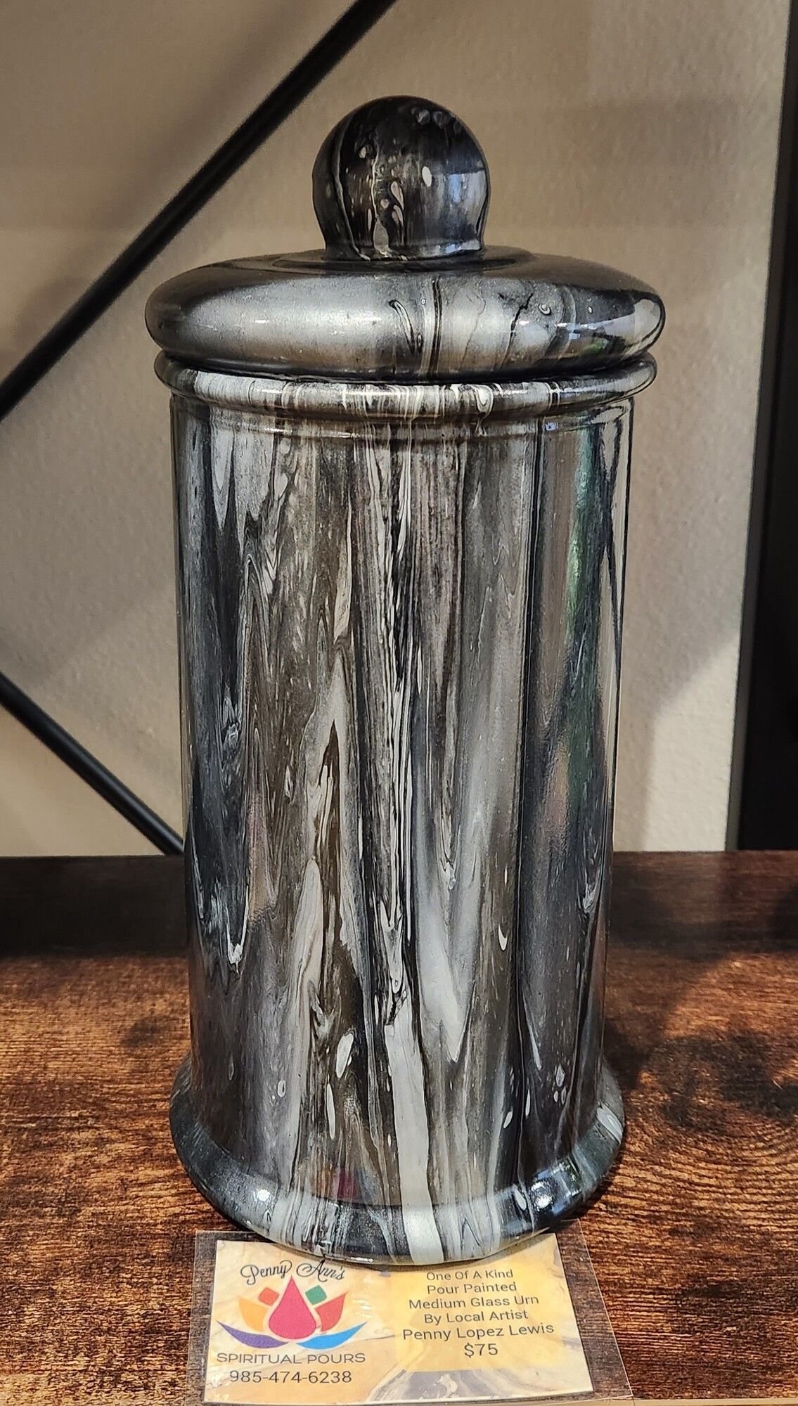 Tall, silver and black painted jar with a lid, sitting on a wooden surface. A decorative card sits in front.