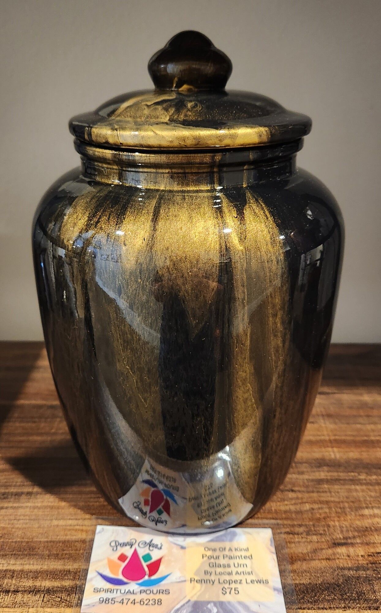 Black and gold ceramic jar with lid, sitting on a wooden surface.