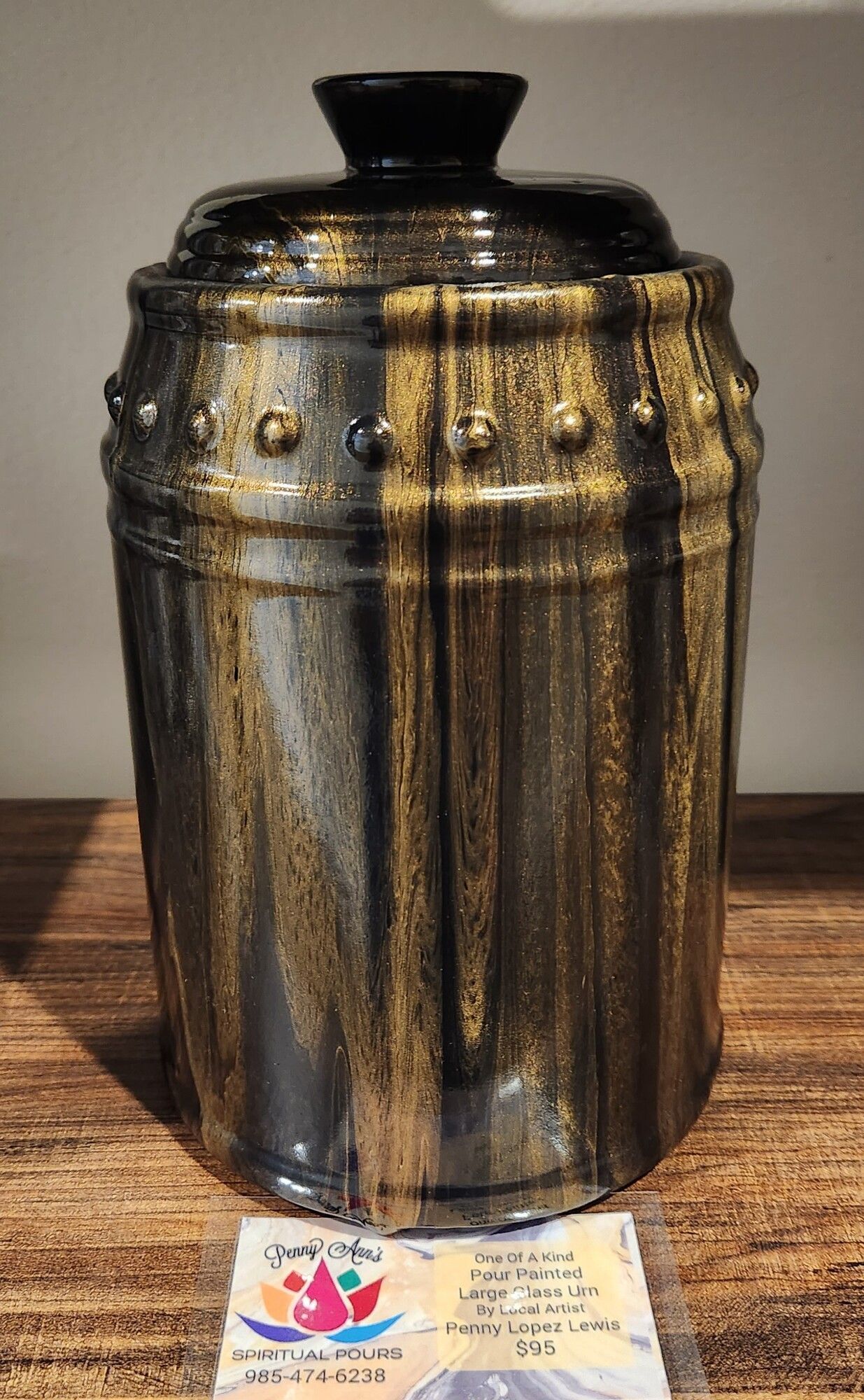 Black and gold ceramic jar with lid, on a wooden surface.
