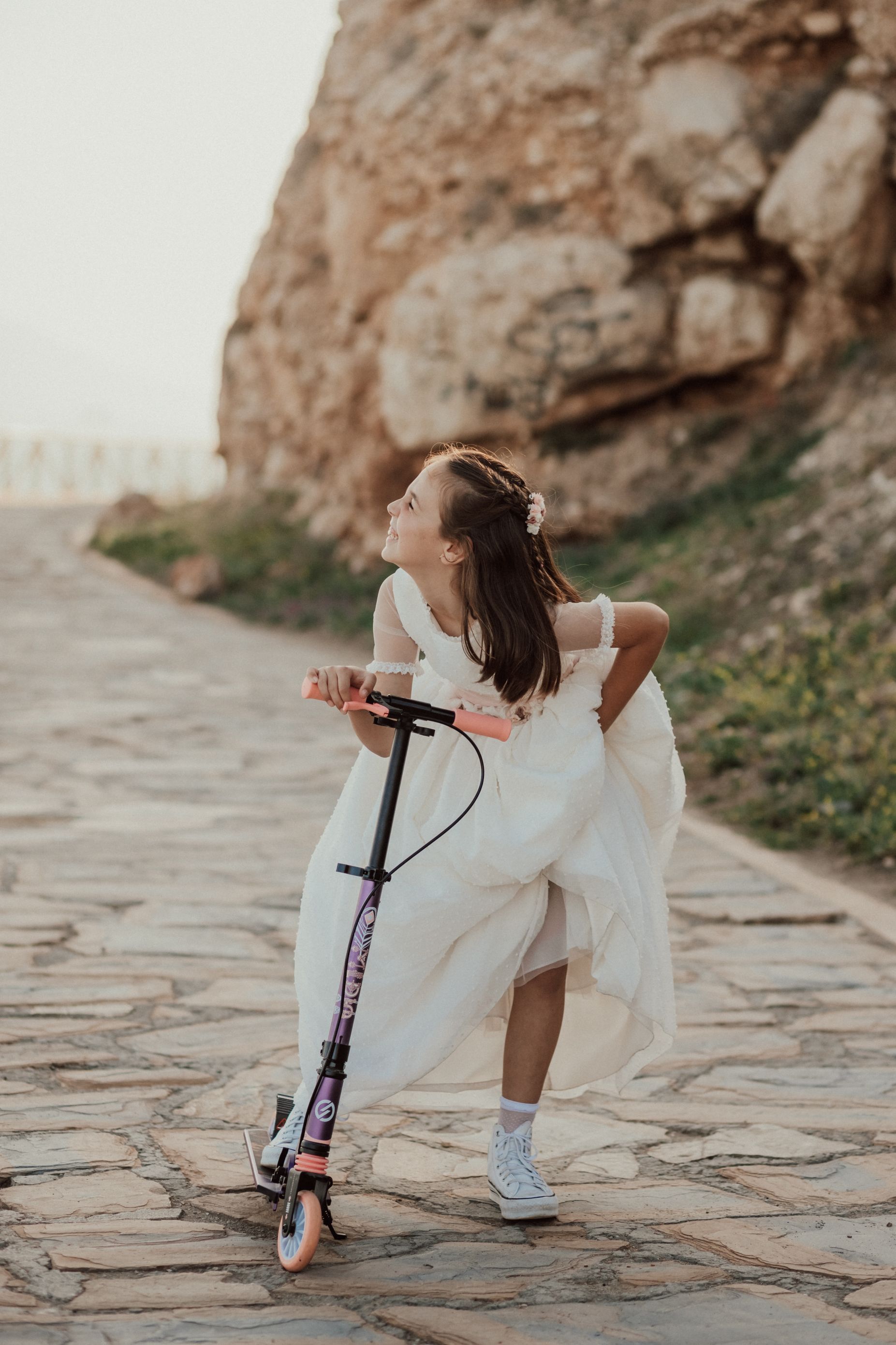 Una niña con un vestido blanco está conduciendo un scooter.