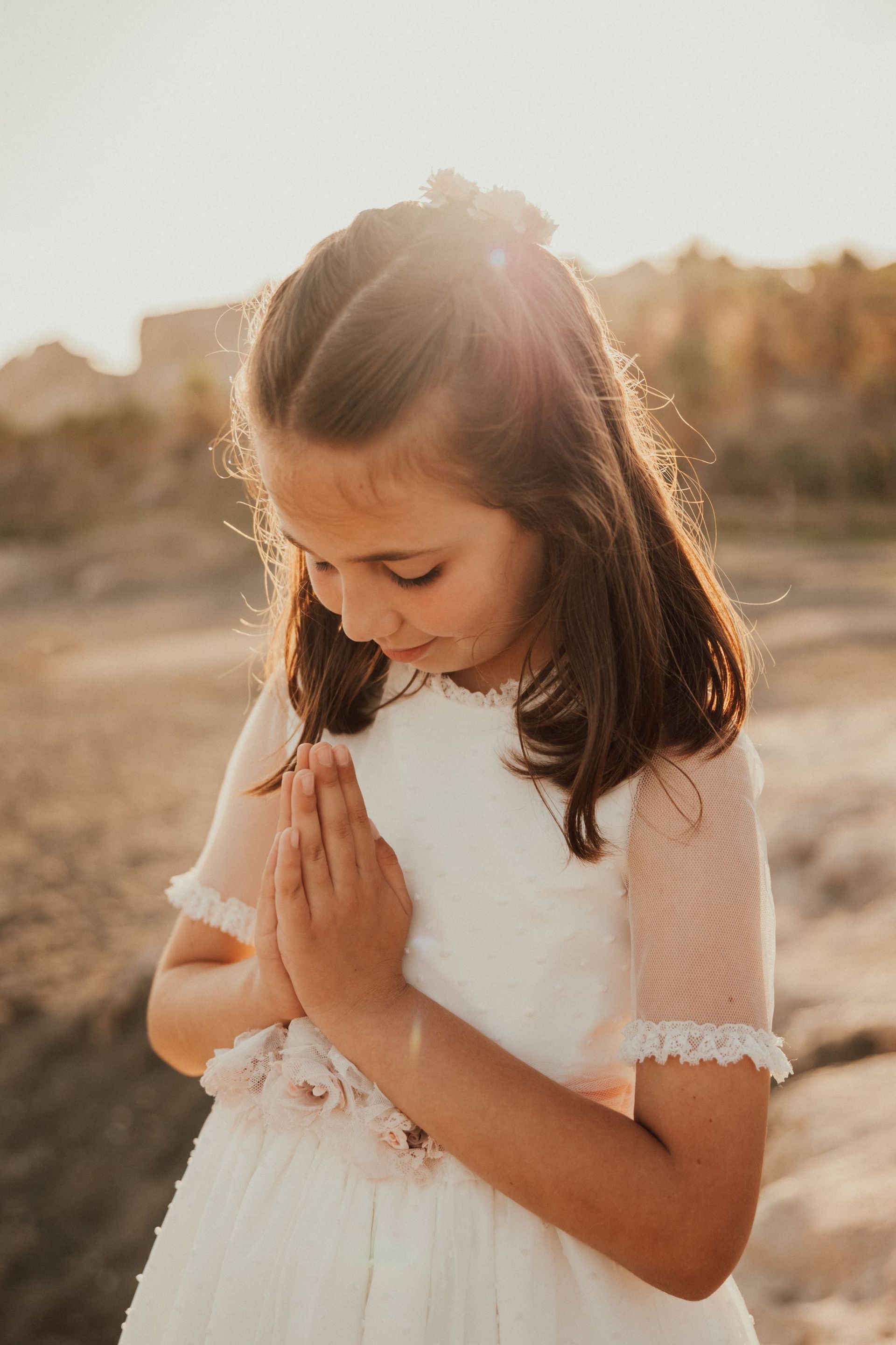 Una niña con un vestido blanco está rezando en la playa.