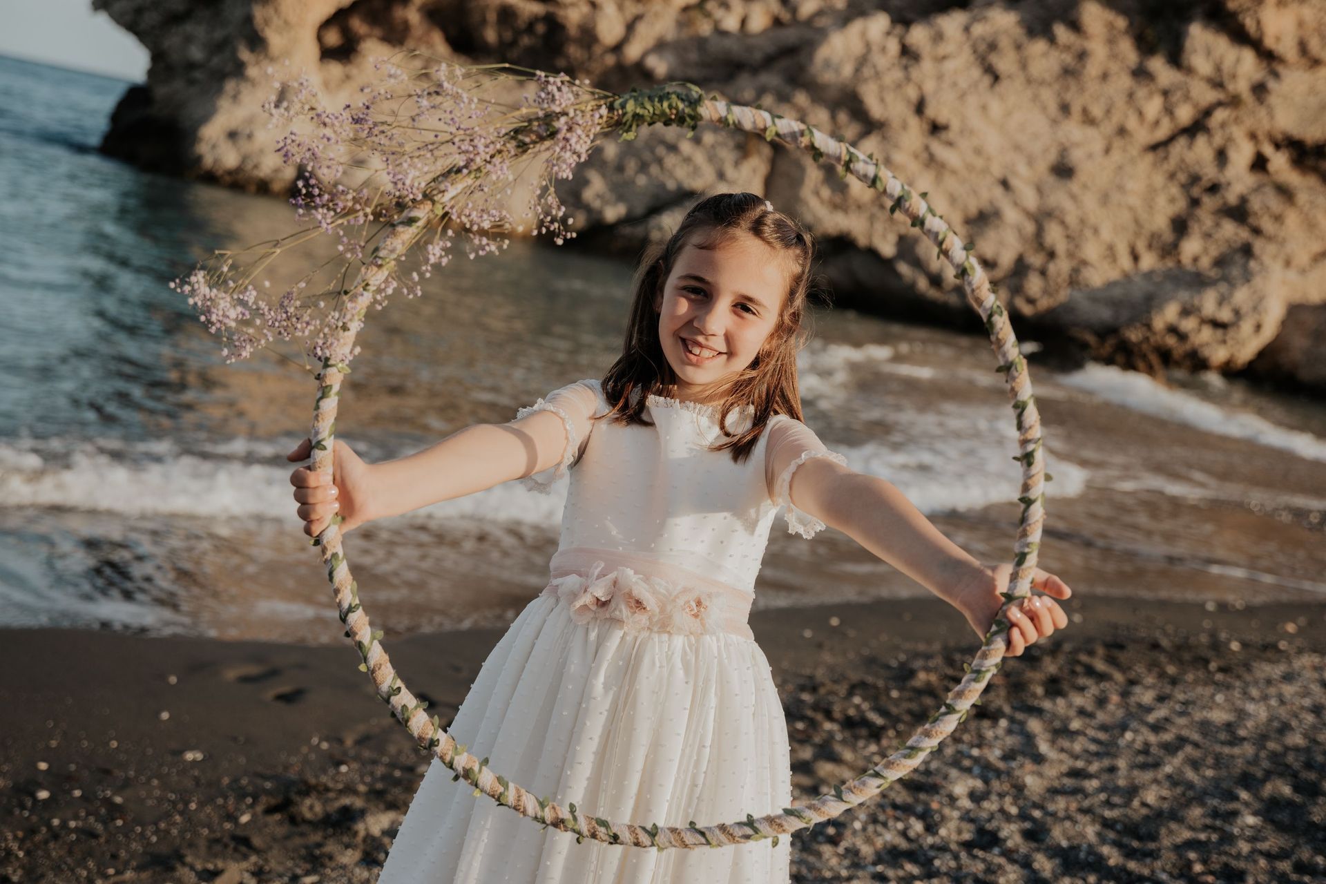 Una niña con un vestido blanco sostiene un aro de hula hula en la playa.
