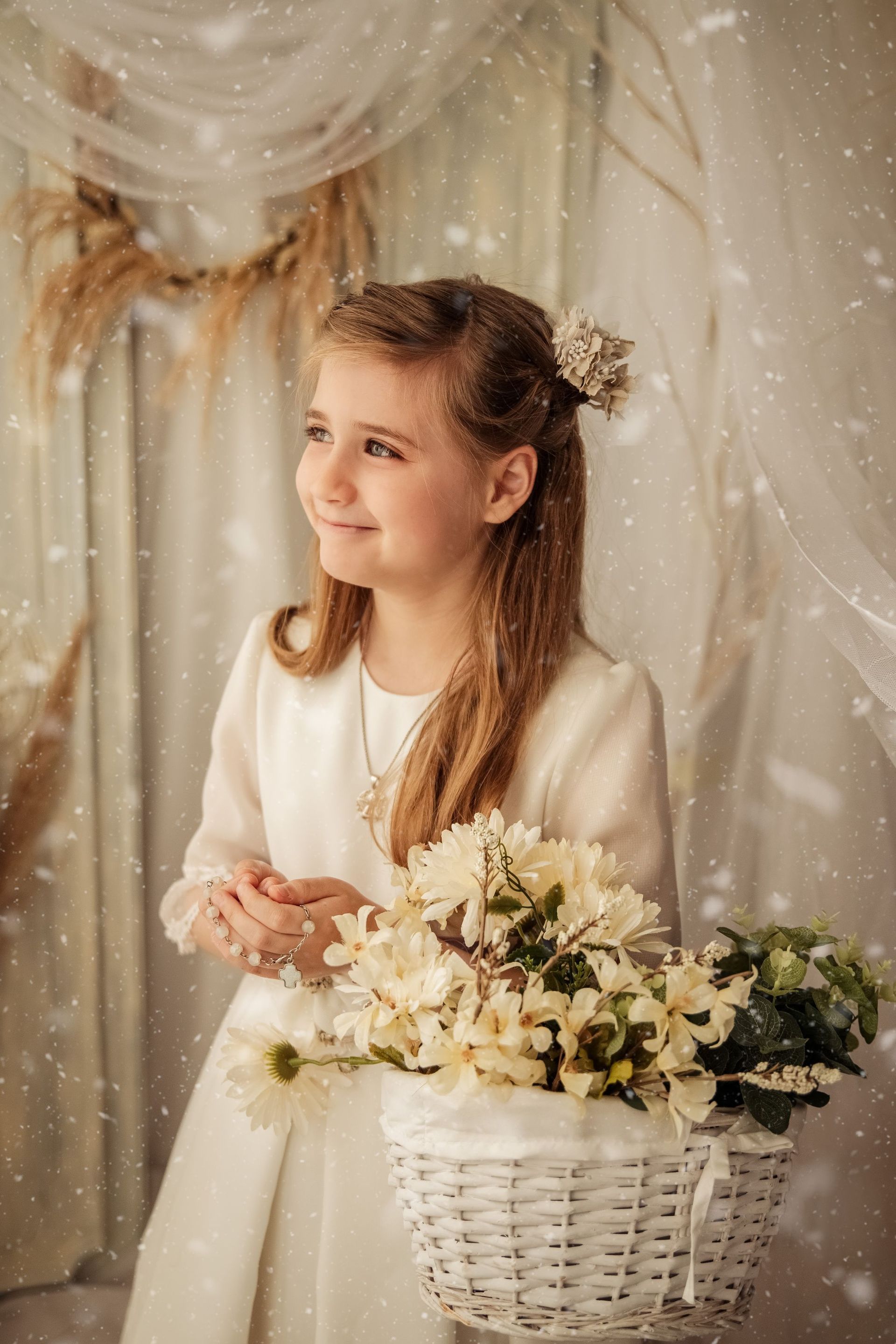 Una niña con un vestido blanco sostiene una canasta de flores.