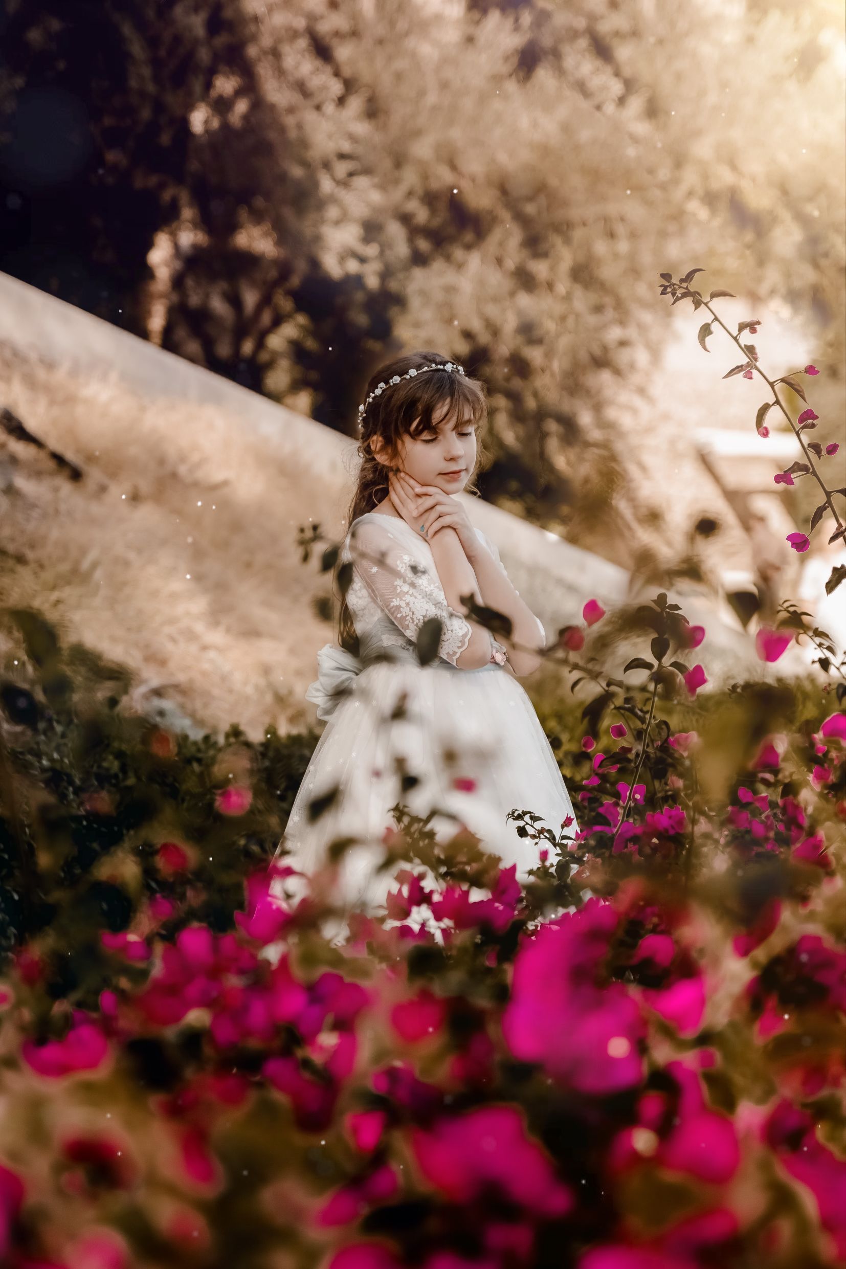 Una niña con un vestido blanco está parada en un campo de flores rosas.
