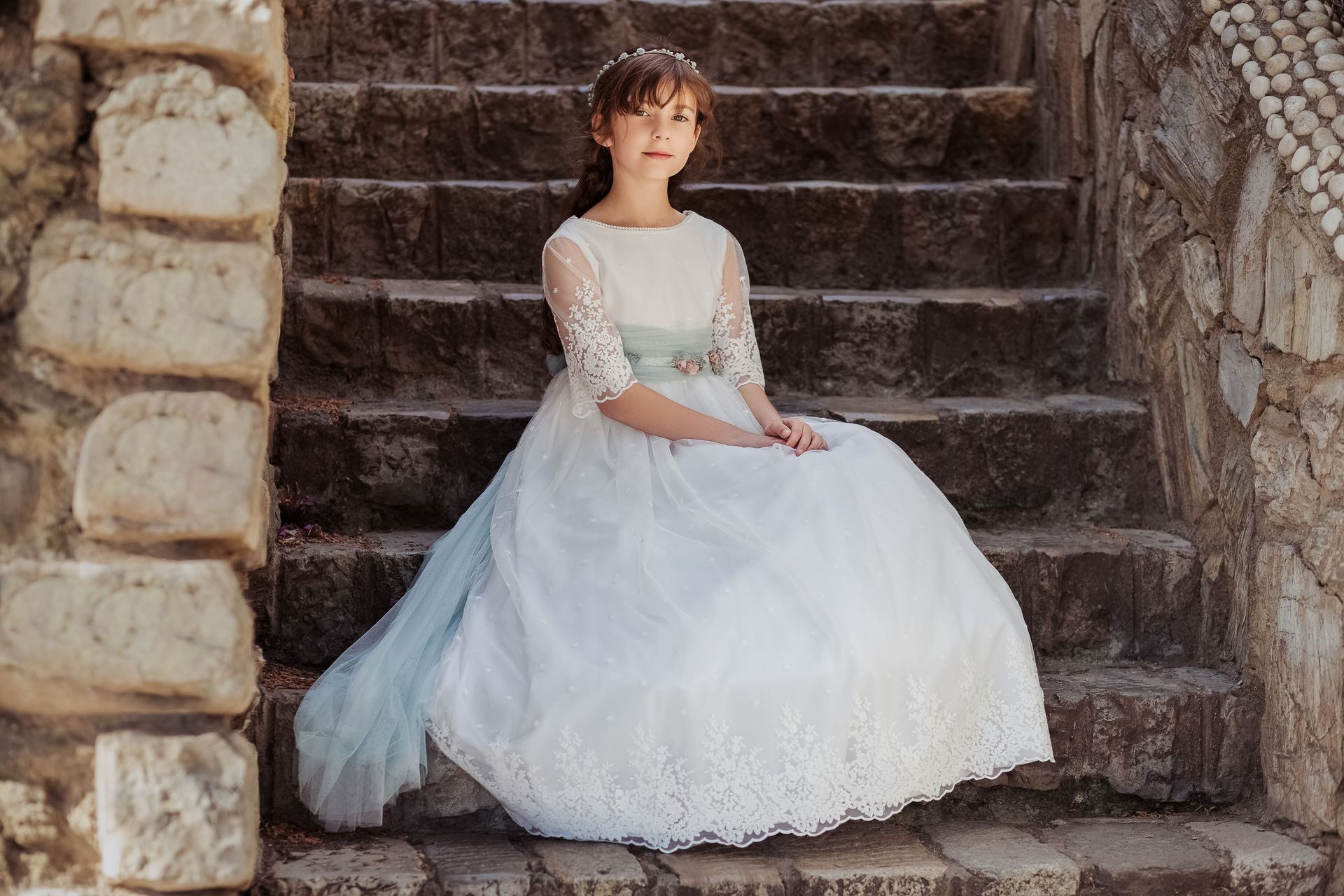 Una niña con un vestido blanco está sentada en unas escaleras.