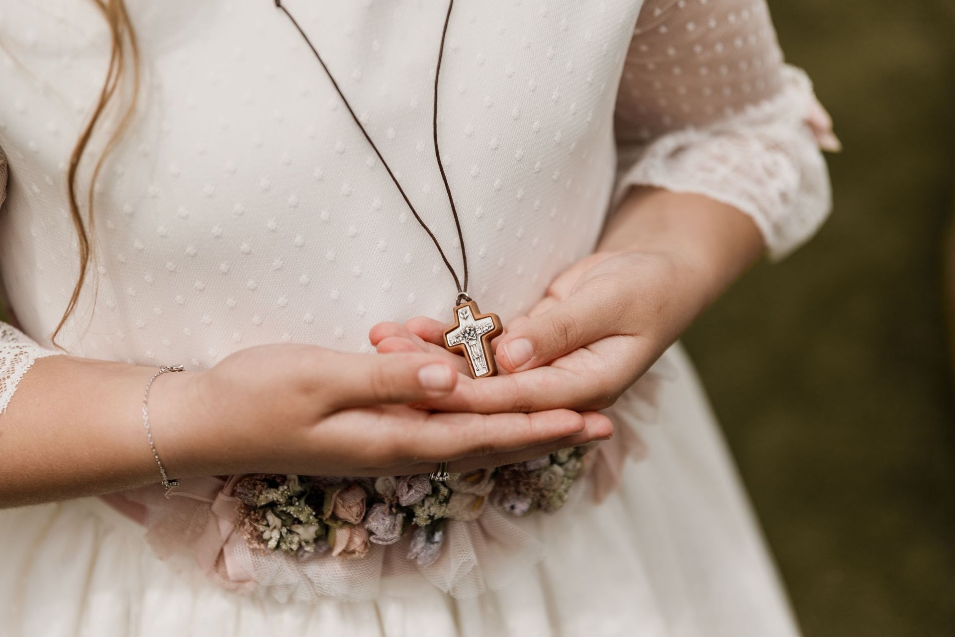 Una niña con un vestido blanco sostiene una cruz en sus manos.