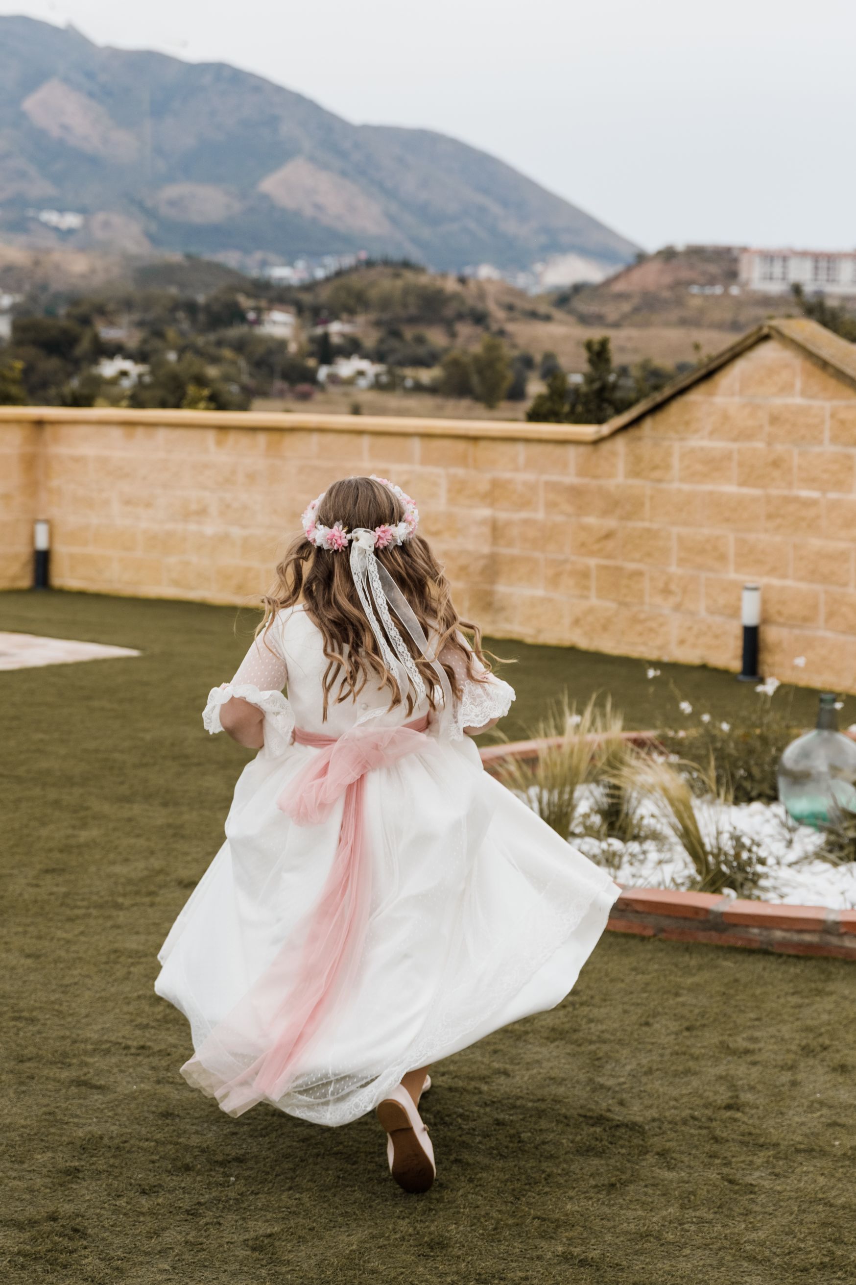 Una niña con un vestido blanco corre por un exuberante campo verde.