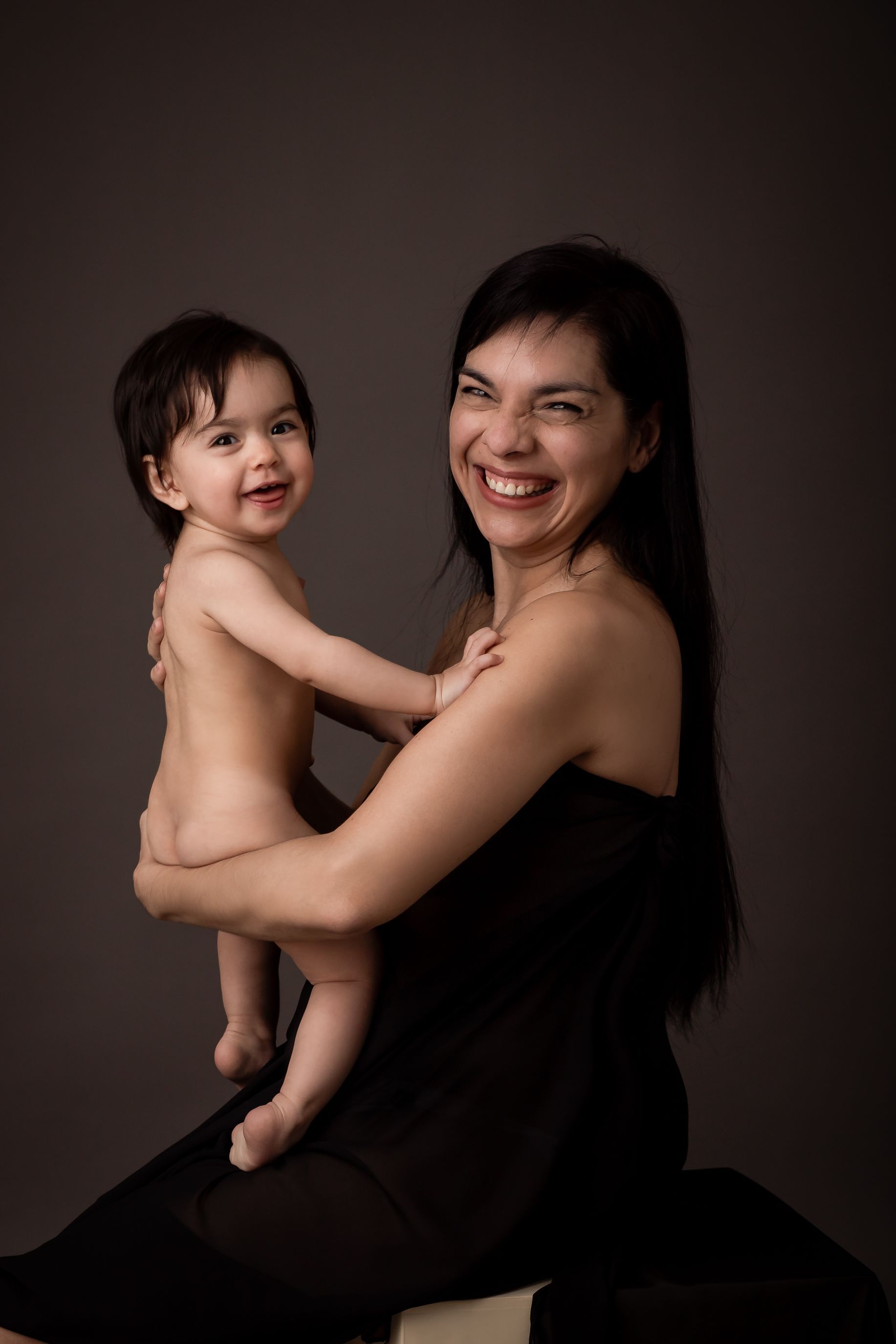 Mujer sosteniendo un bebé sonriente; ambos miran a la cámara.