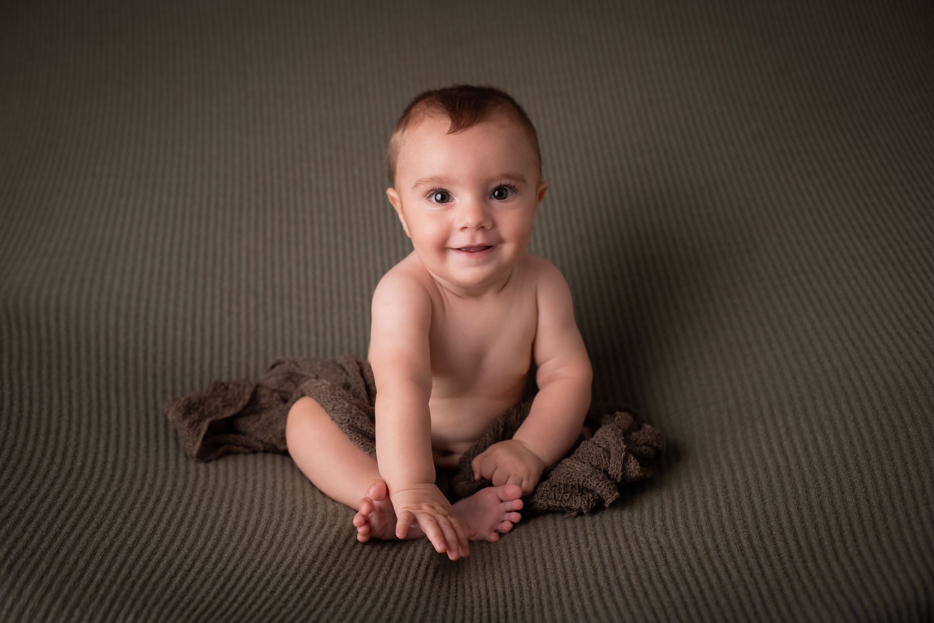 Un bebé está sentado sobre una manta y sonríe a la cámara.