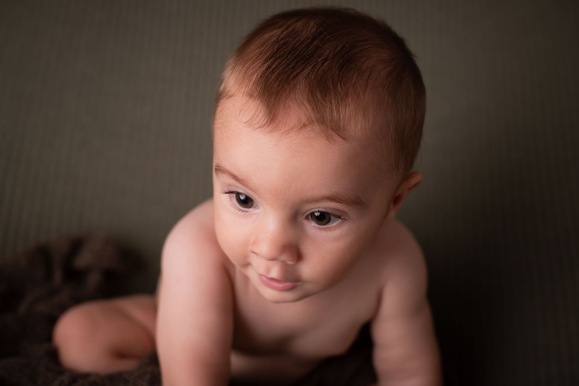 Un bebé gatea sobre una manta y mira a la cámara.