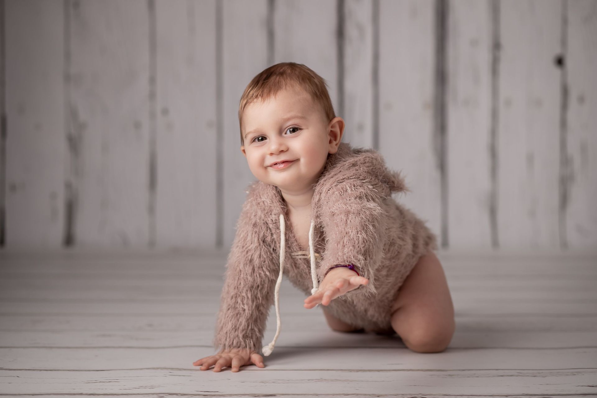 Un bebé gatea por el suelo vistiendo un suéter peludo.