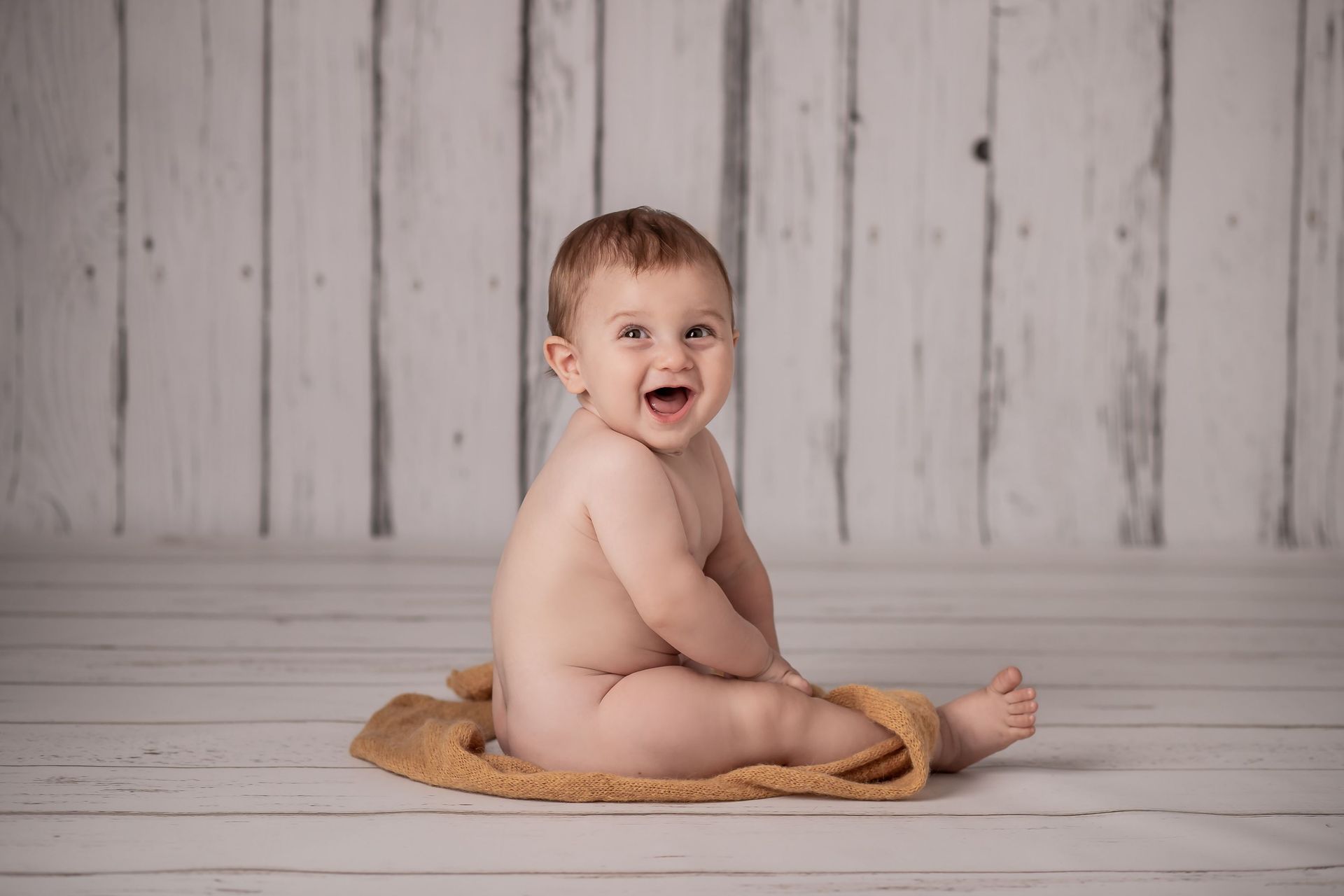 Un bebé está sentado en un piso de madera y sonriendo.