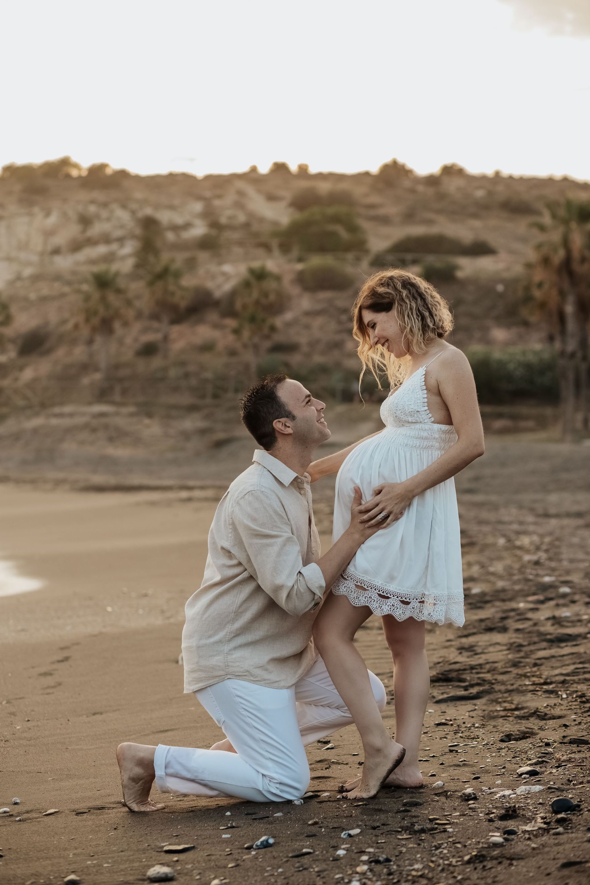 Un hombre está arrodillado junto a una mujer embarazada en una playa.