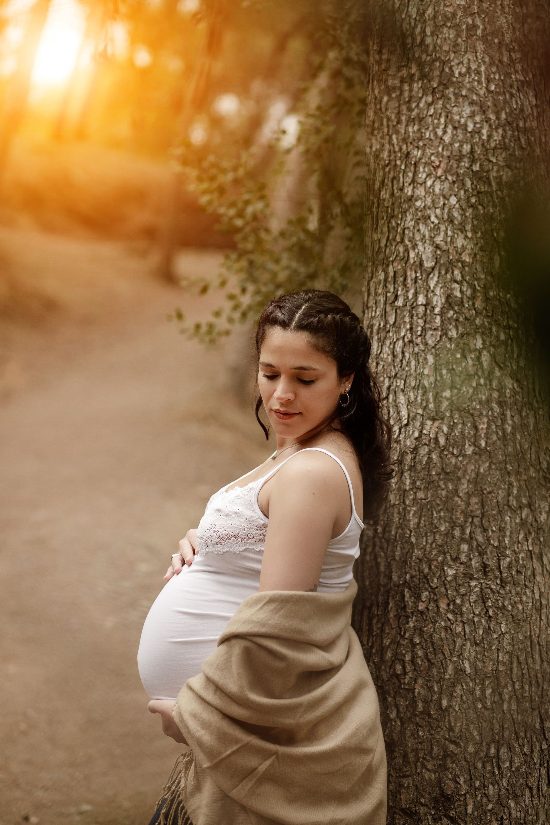 Una mujer embarazada está apoyada contra un árbol mientras sostiene su vientre.