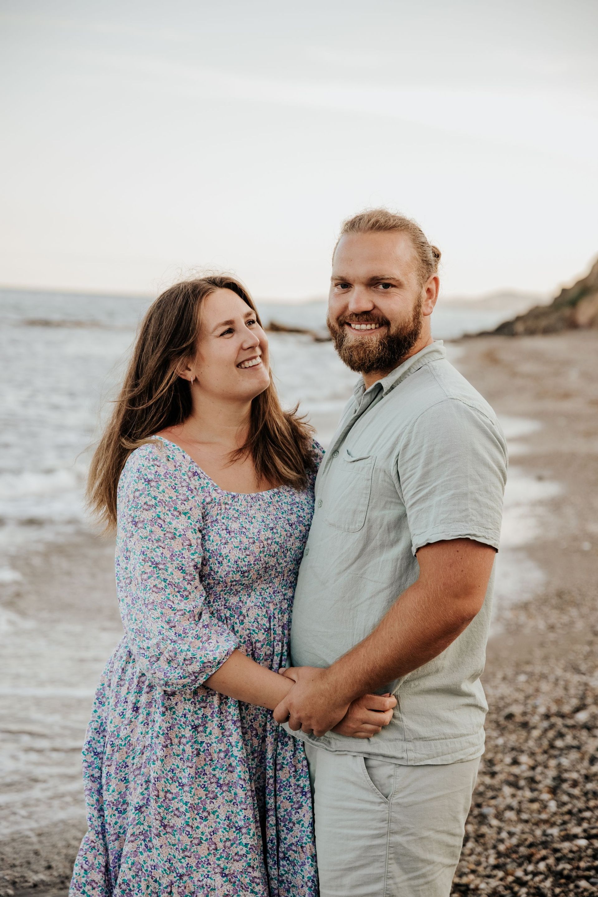 Un hombre y una mujer están parados en una playa tomados de la mano.