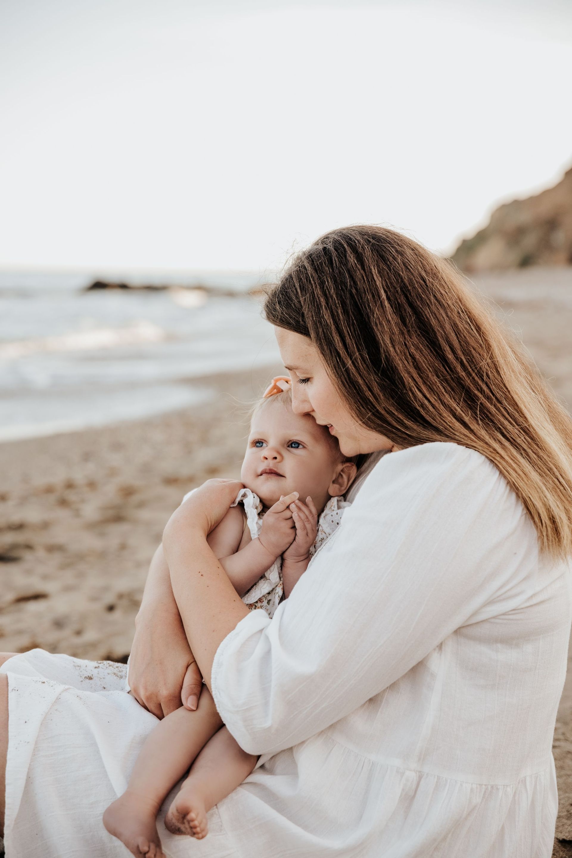 Una mujer sostiene un bebé en la playa.