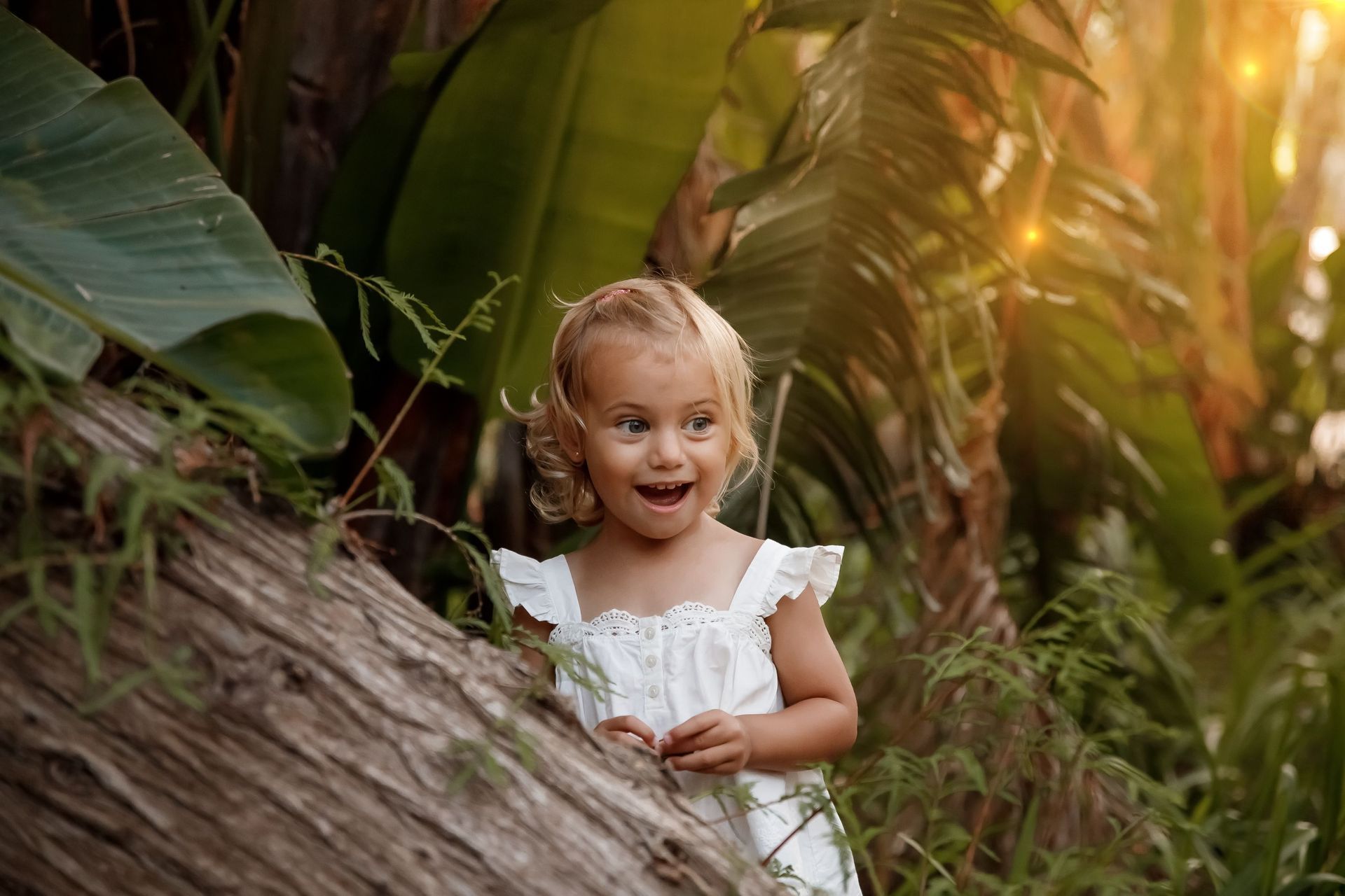 Una niña con un vestido blanco está parada junto a un árbol en el bosque.