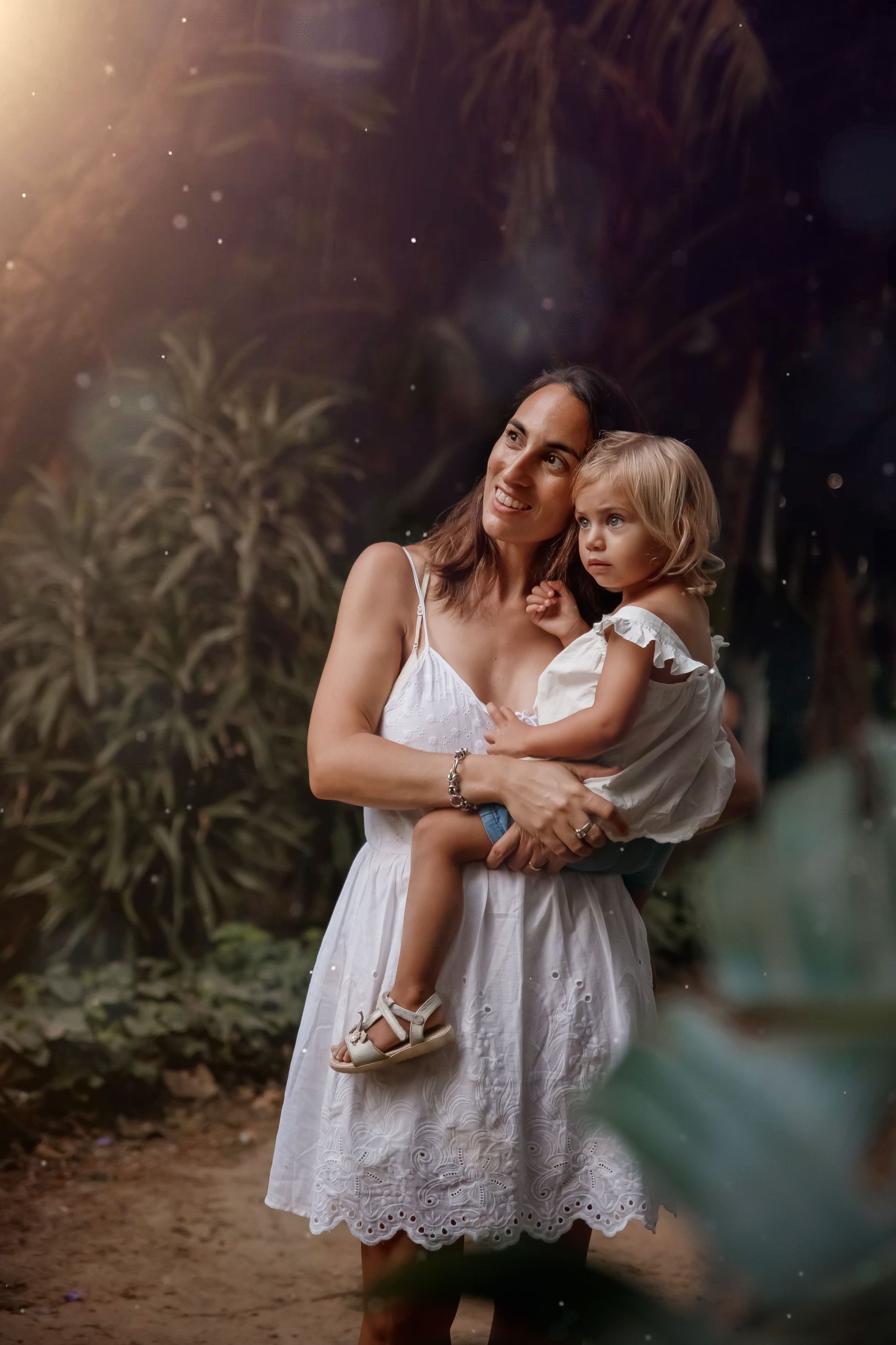 Una mujer con un vestido blanco sostiene a una niña en sus brazos.