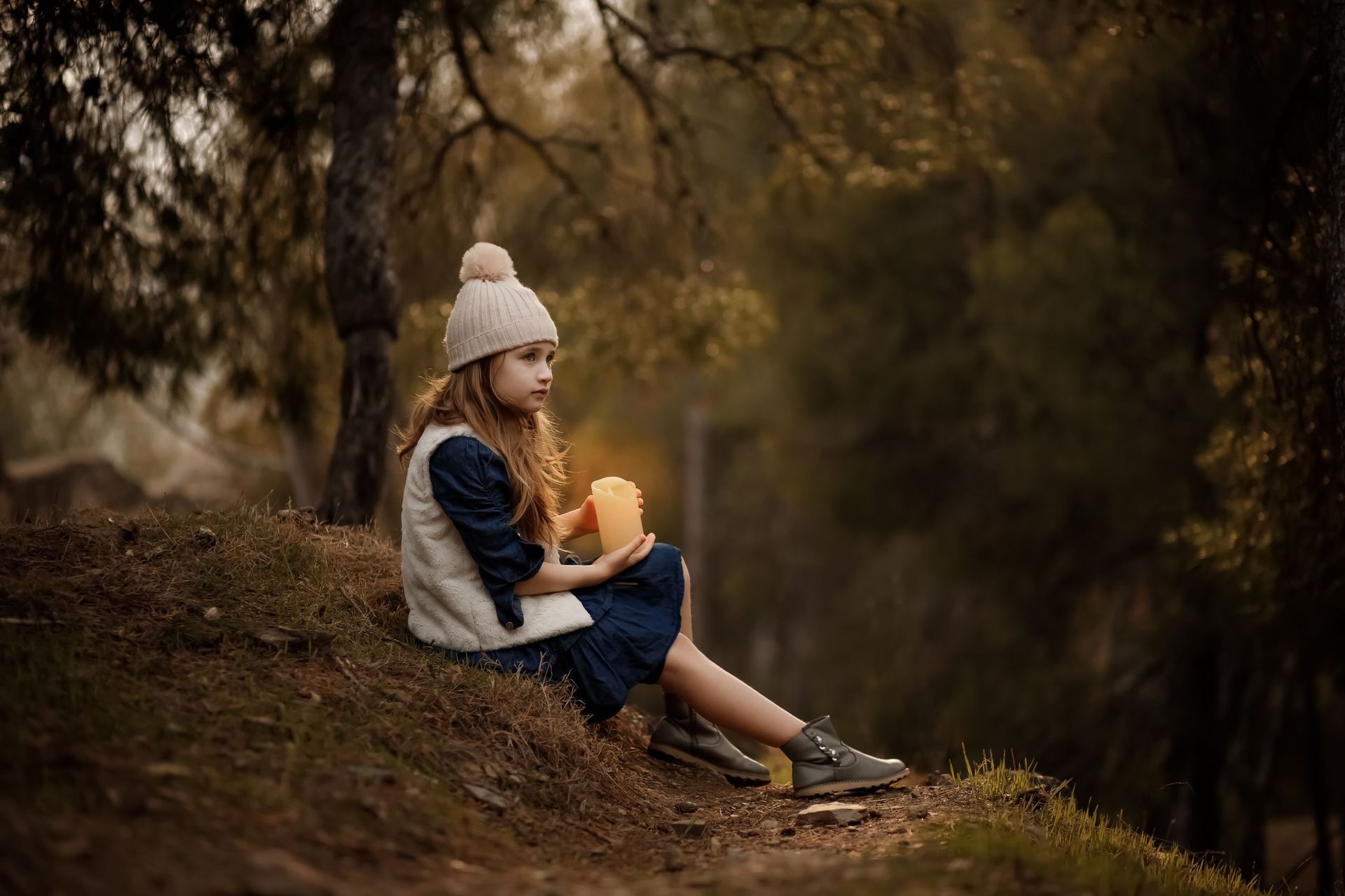 Una niña está sentada en una colina en el bosque sosteniendo una calabaza.