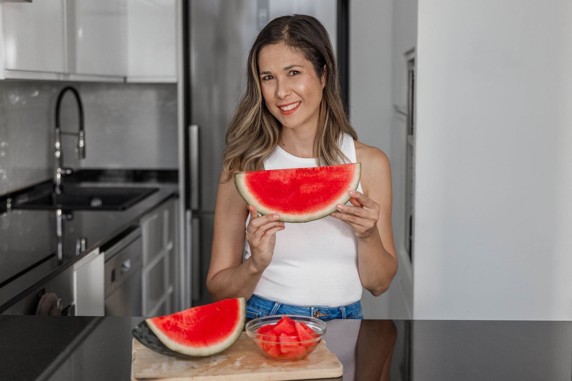 Una mujer está comiendo una rodaja de sandía en una cocina.