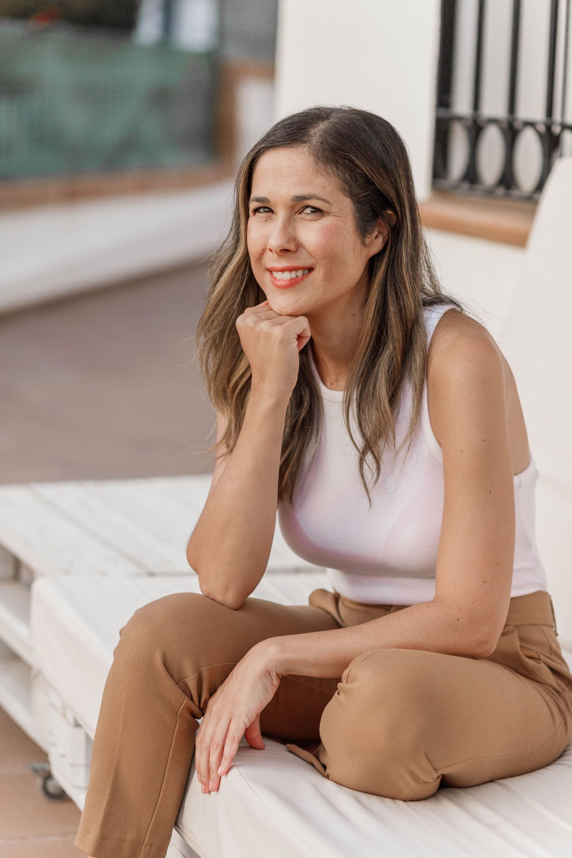 Una mujer está sentada en un sofá blanco con la mano en la barbilla.