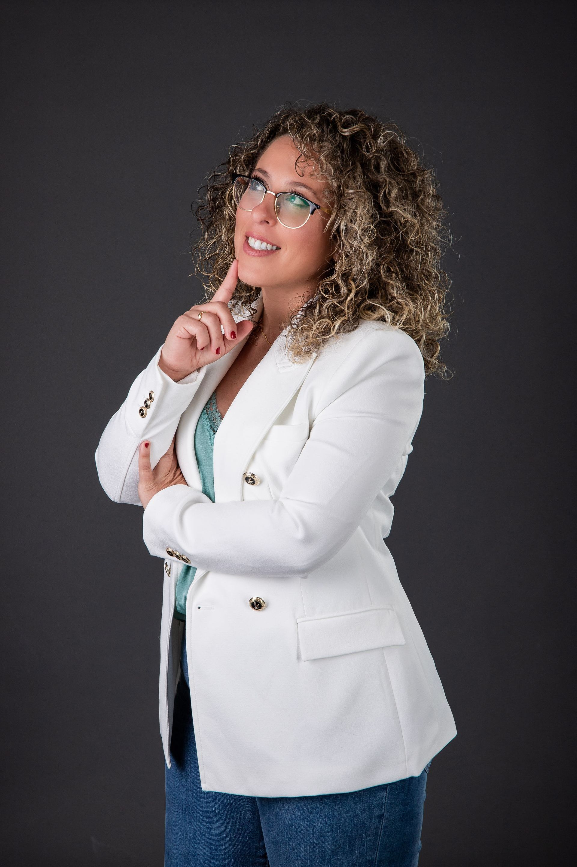 Una mujer que lleva gafas y una chaqueta blanca está parada delante de un fondo negro.