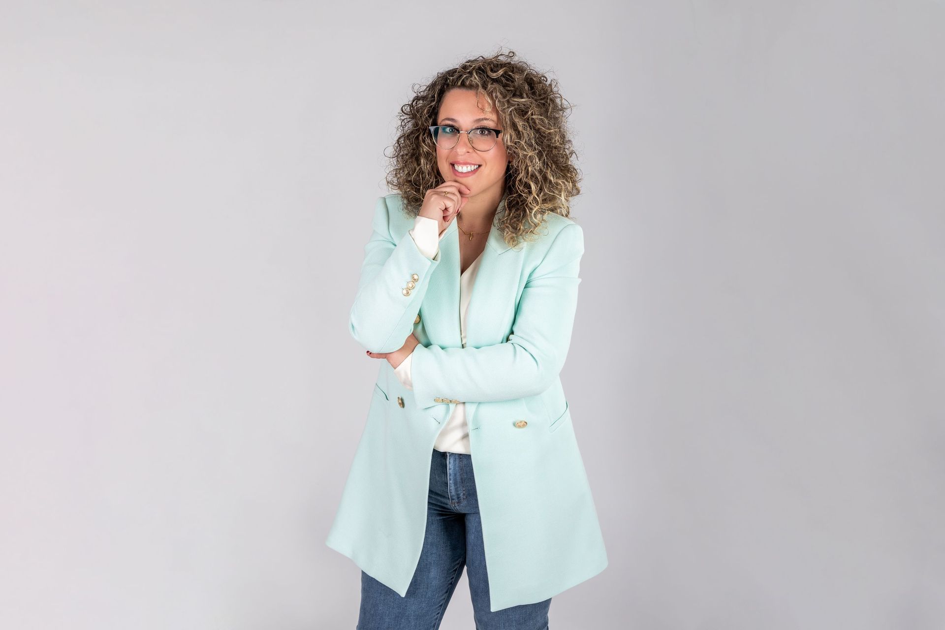 Una mujer que lleva gafas y una chaqueta azul claro está de pie con los brazos cruzados.