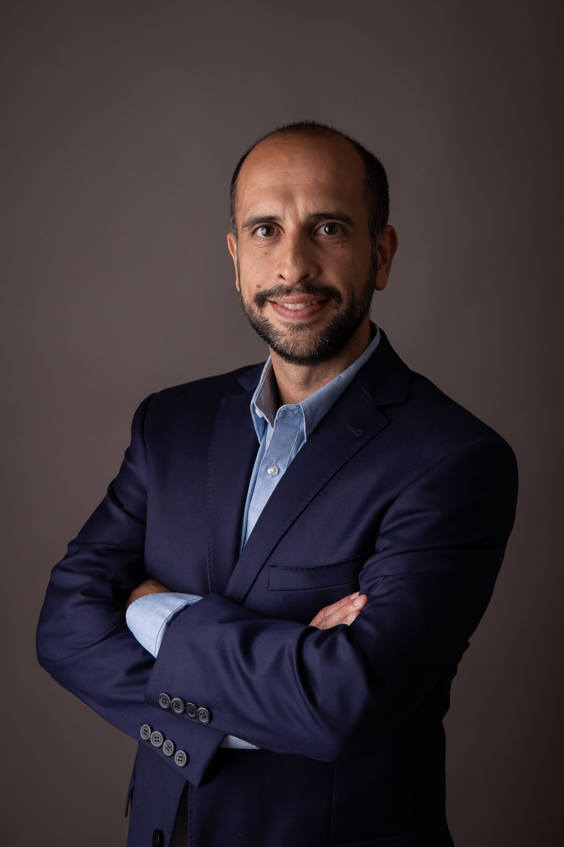 Un hombre con traje está de pie con los brazos cruzados y sonriendo.