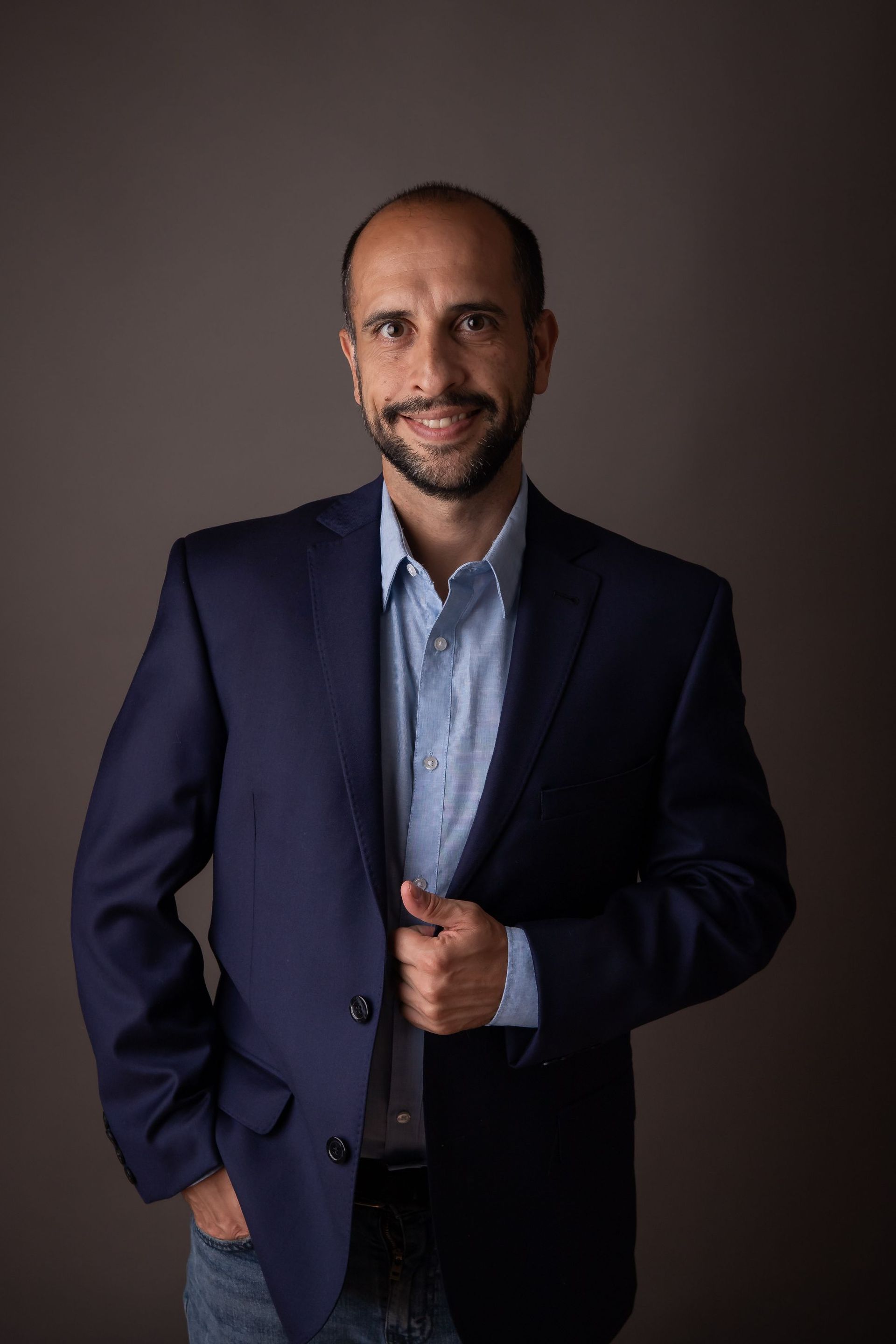 Un hombre con traje y camisa azul está de pie con las manos en los bolsillos.