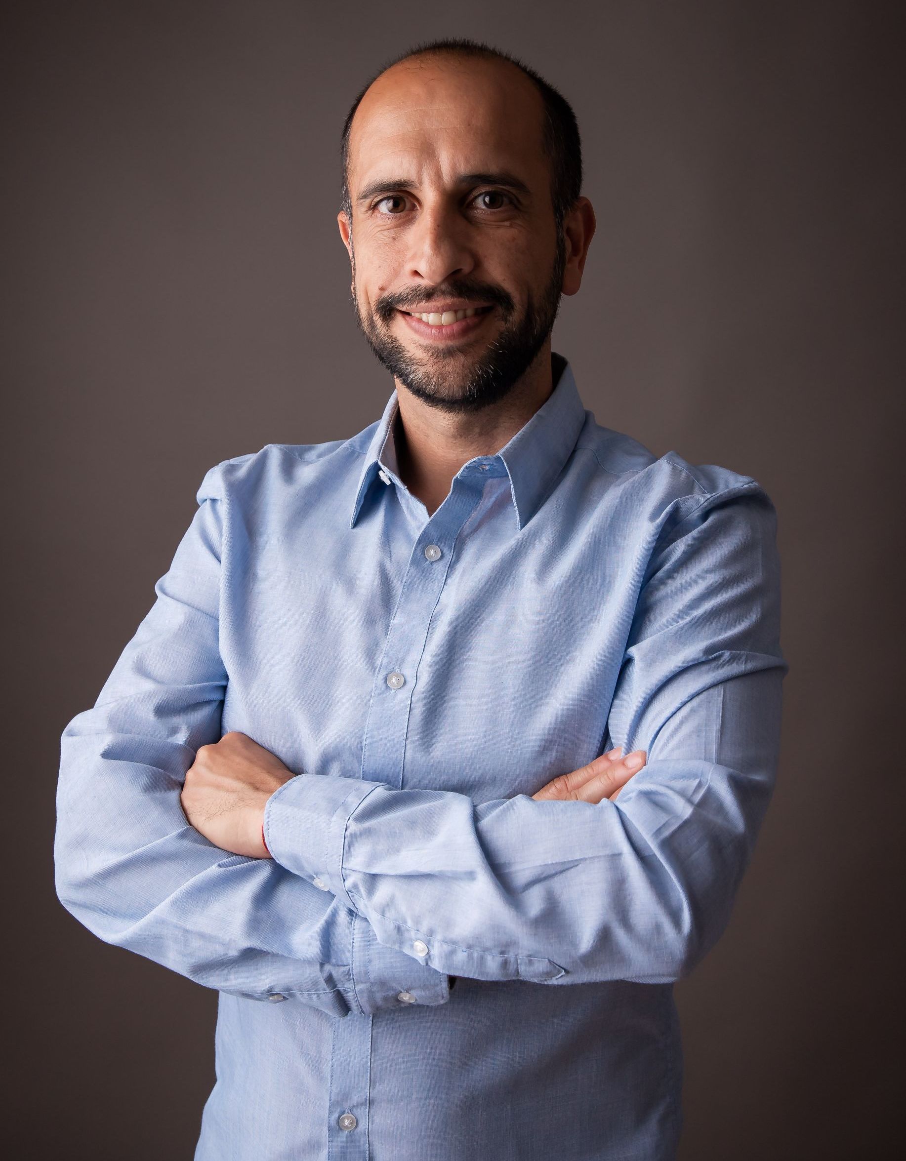 Un hombre con barba está de pie con los brazos cruzados y sonriendo.