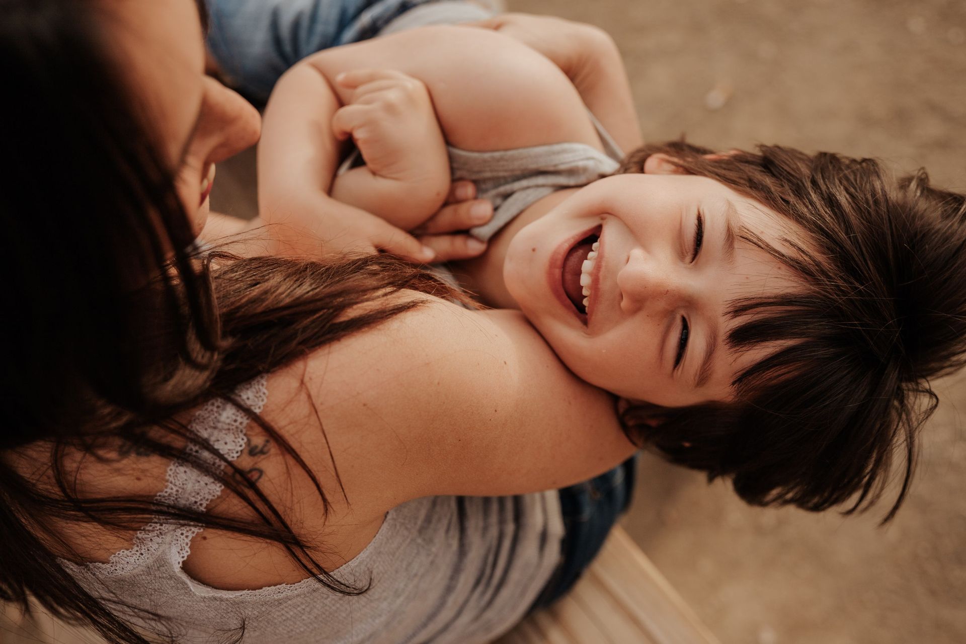 Una mujer yace en el suelo sosteniendo a un niño pequeño que se ríe.