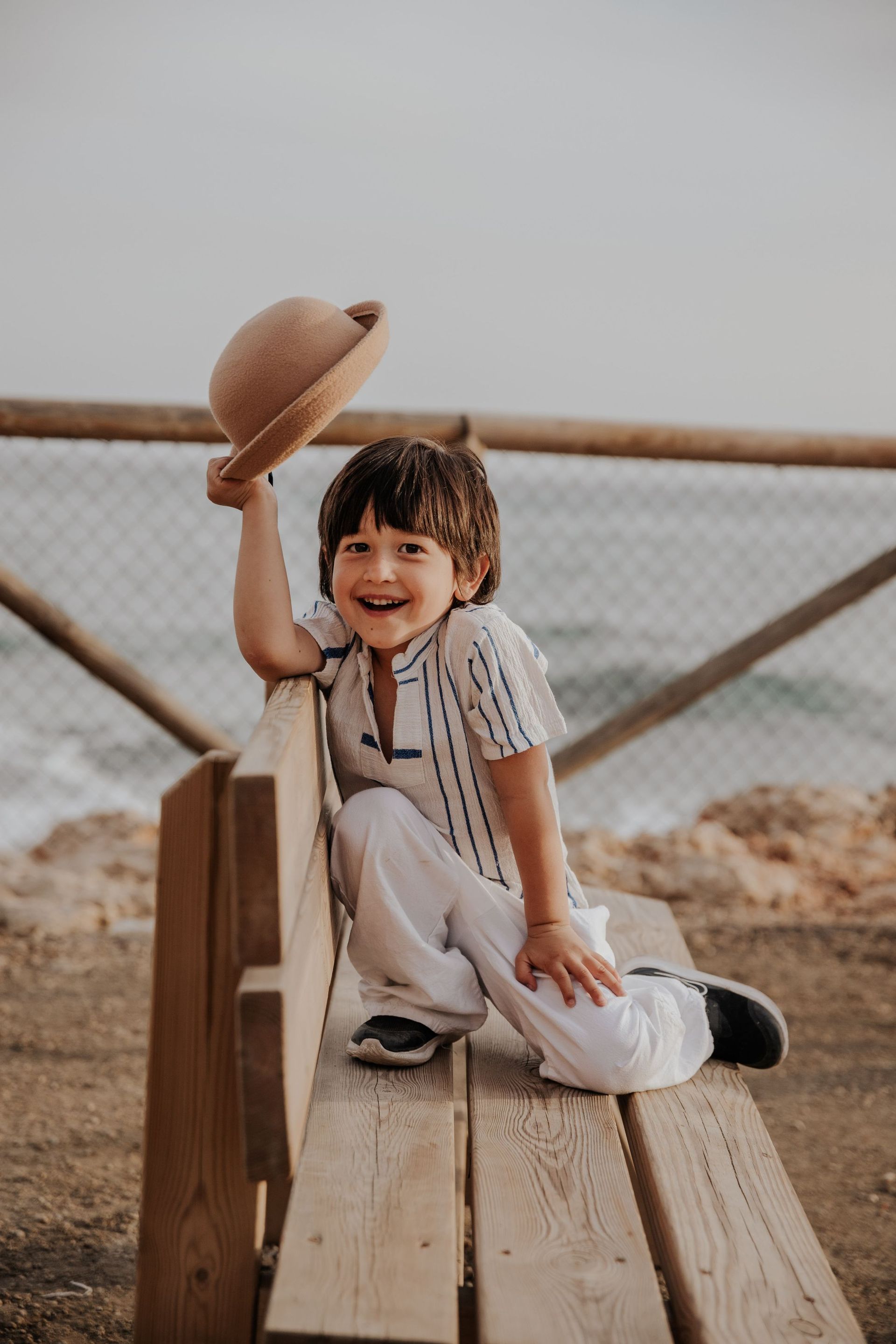 Un niño pequeño está sentado en un banco de madera sosteniendo un sombrero en su mano.