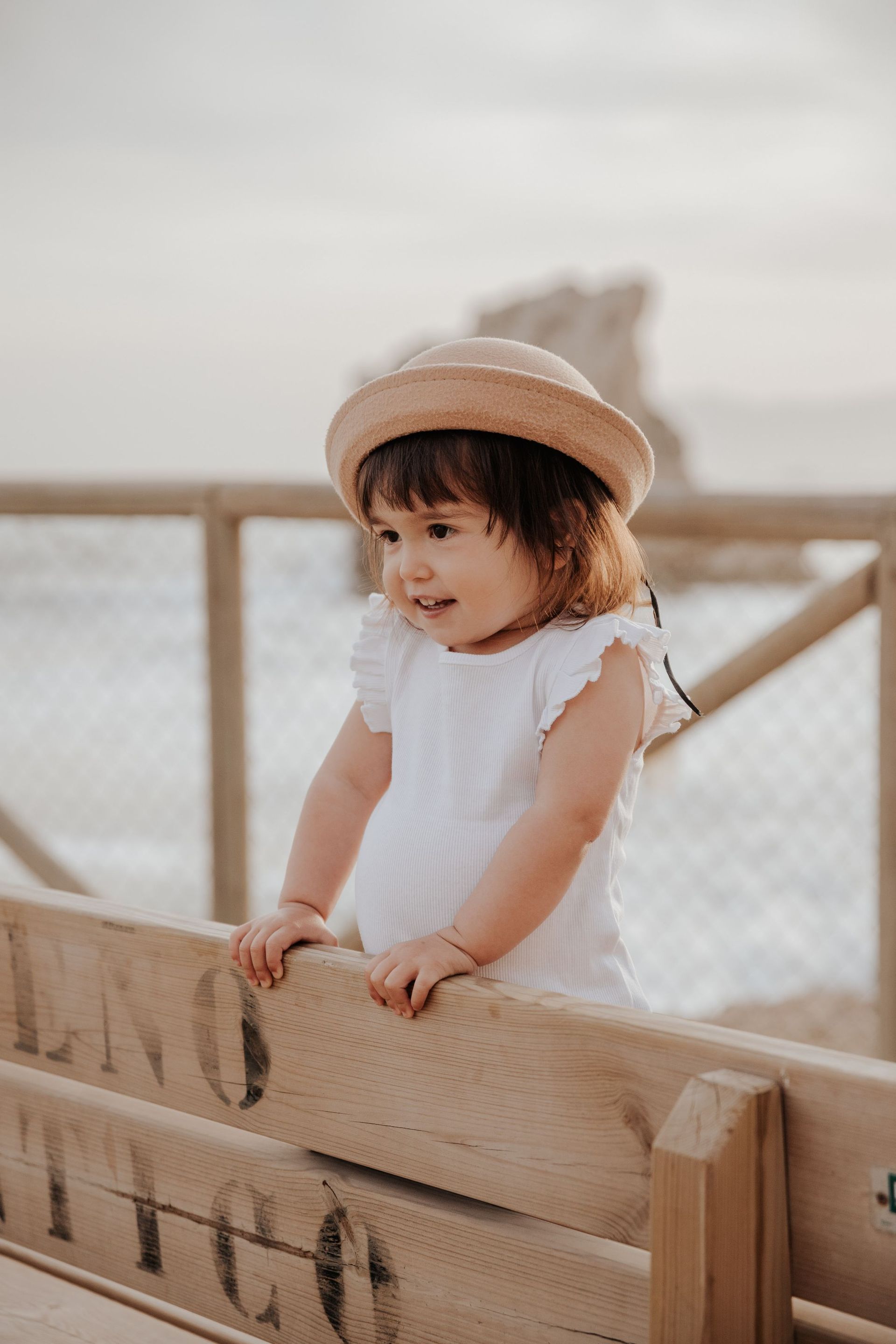Una niña que lleva un sombrero y un vestido blanco está parada sobre una valla de madera.
