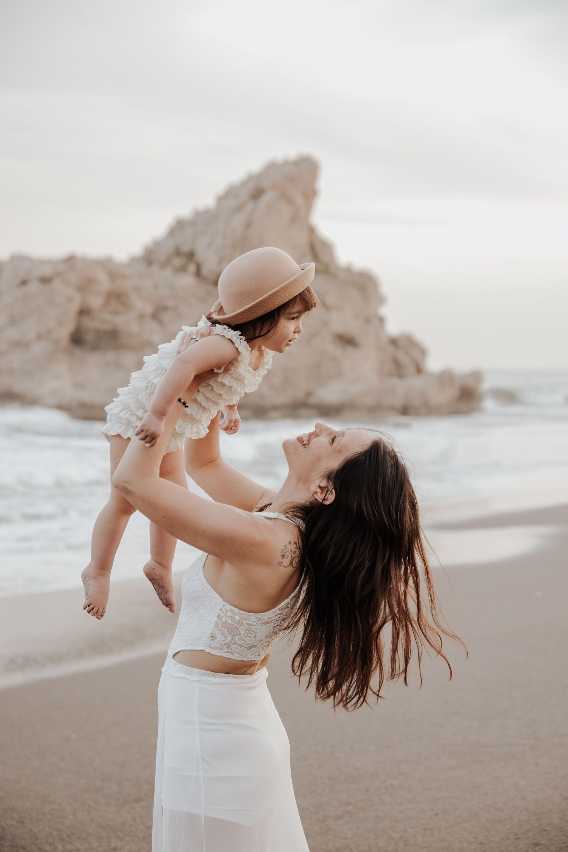 Una mujer sostiene a una niña en sus brazos en la playa.