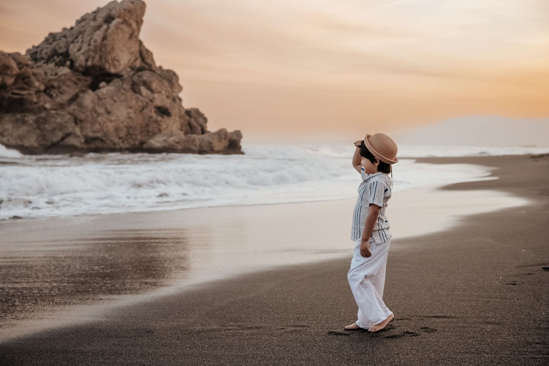 Un niño pequeño está parado en una playa mirando el océano.