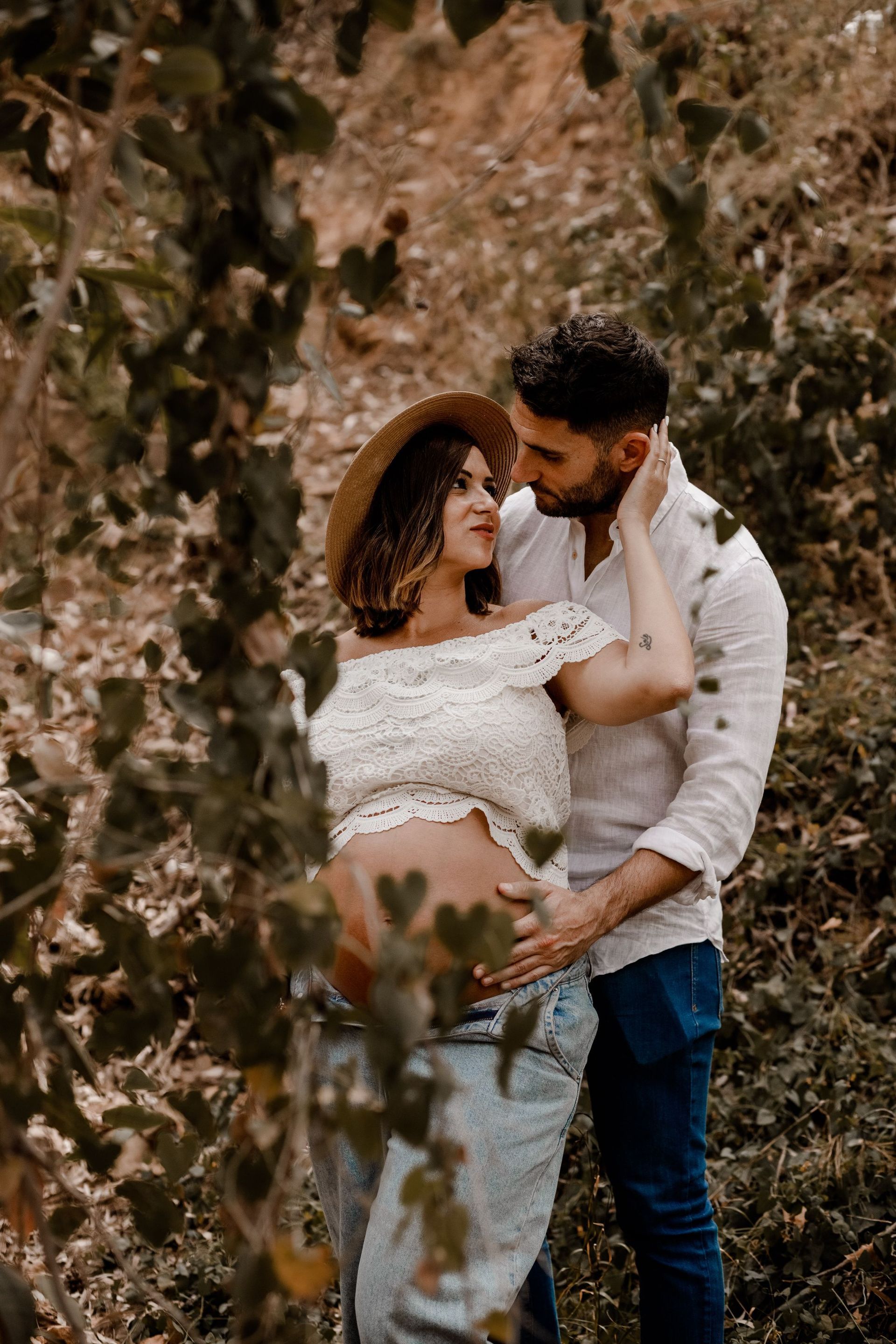 Una mujer embarazada y un hombre se besan en el bosque.