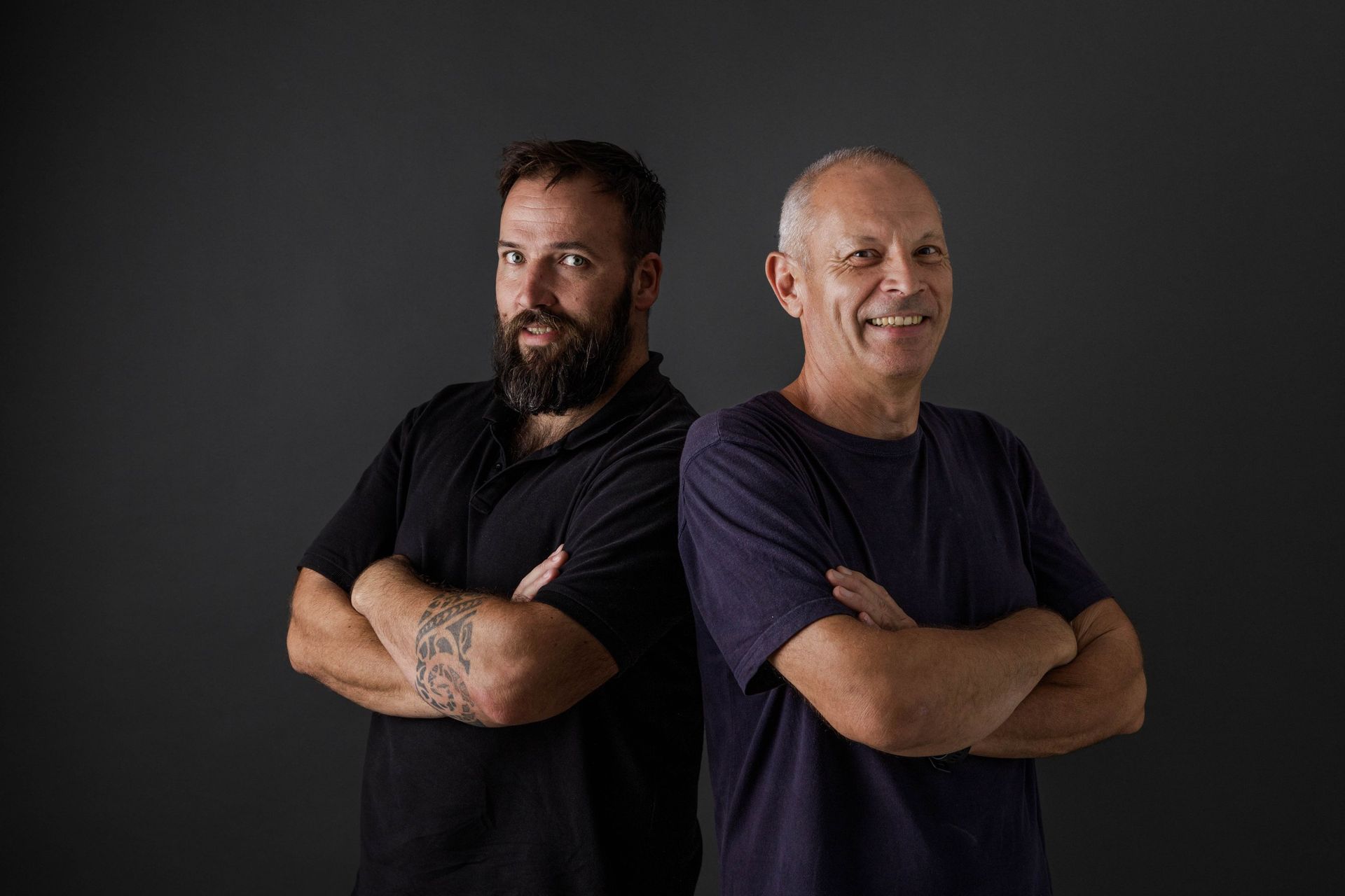 Dos hombres están parados espalda con espalda con los brazos cruzados.