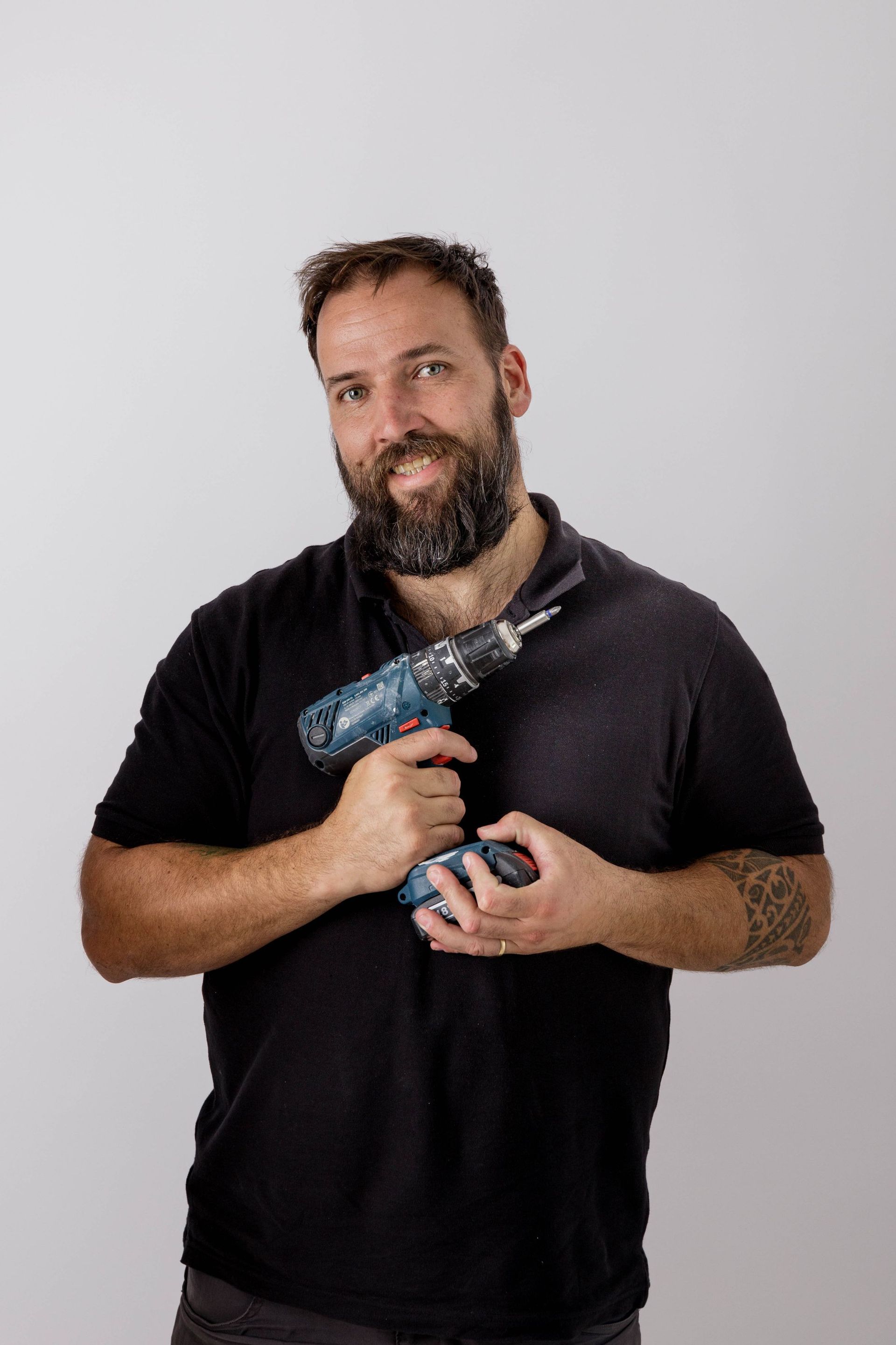 Un hombre con barba sostiene un taladro en su mano.