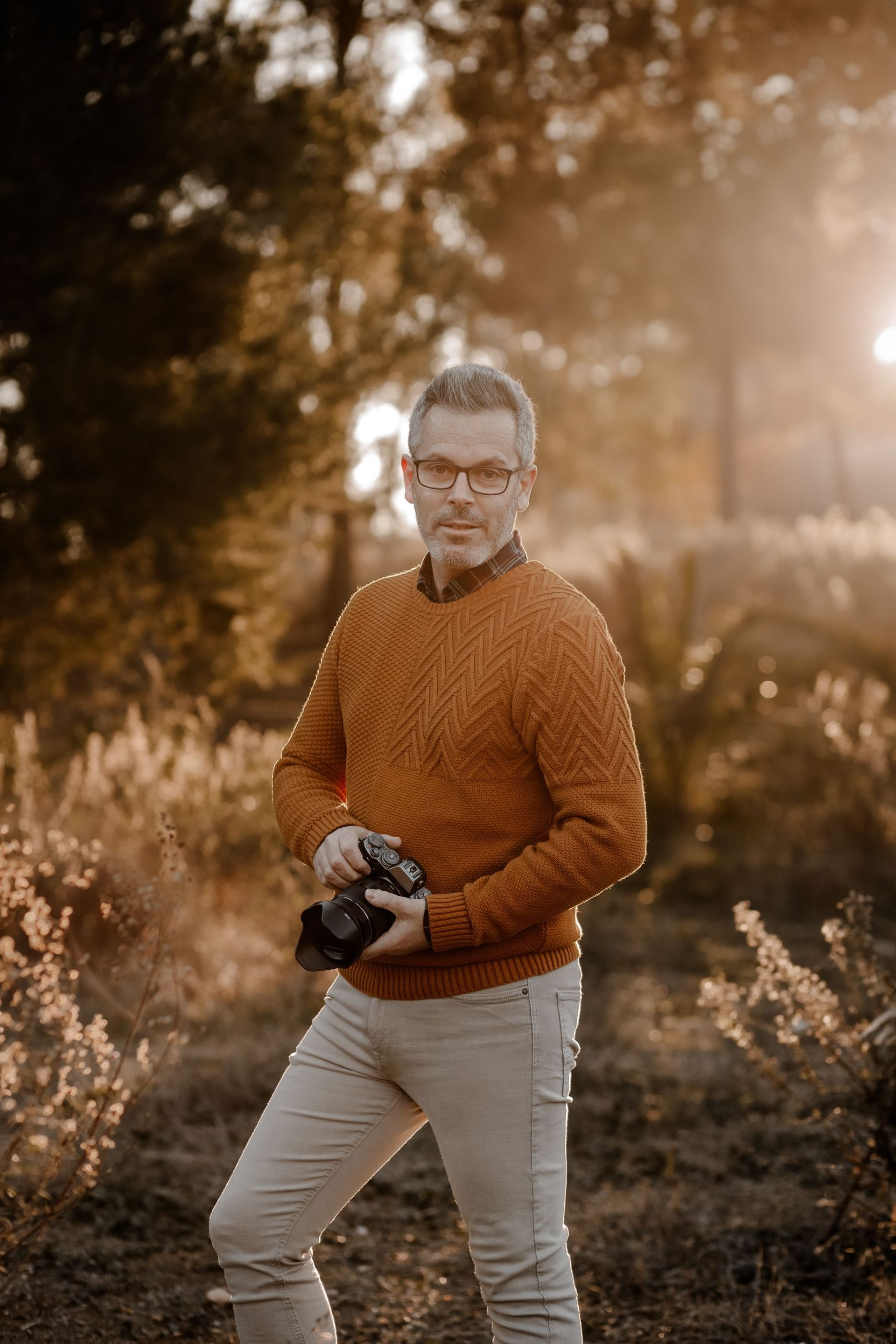 Un hombre con un suéter naranja sostiene una cámara en un campo.