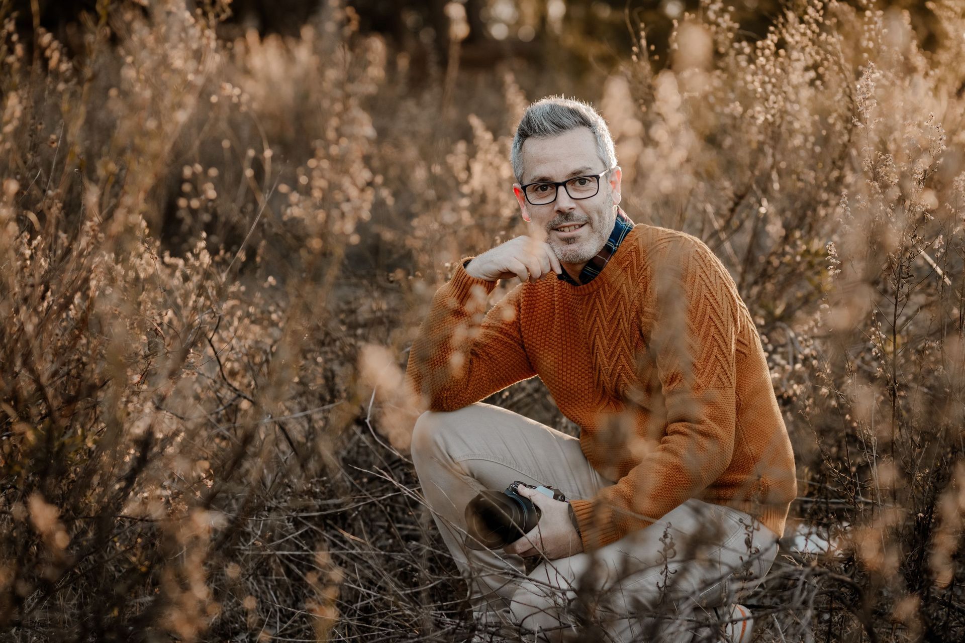 Un hombre está arrodillado en un campo sosteniendo una cámara.