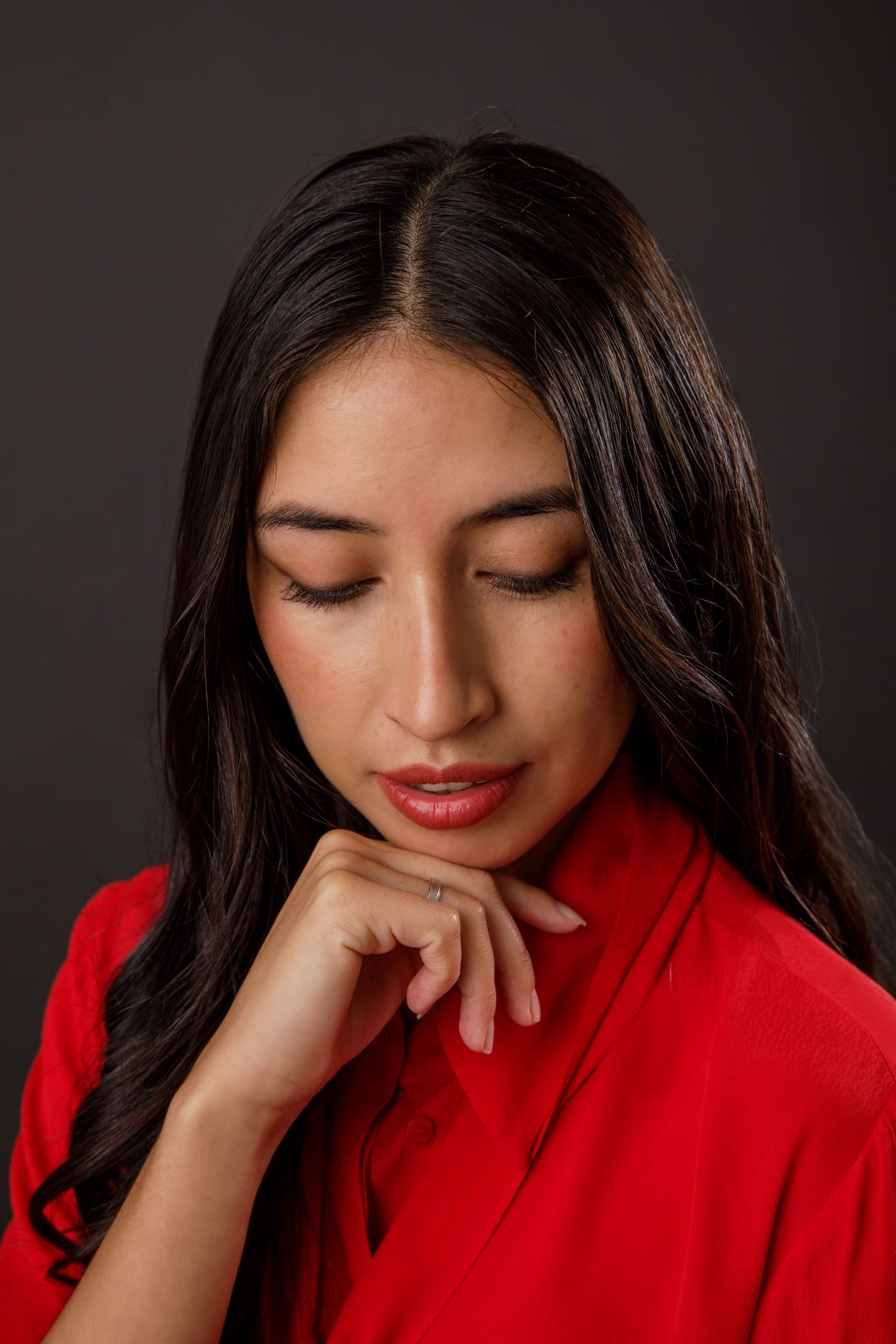 Una mujer con una camisa roja mira hacia abajo con los ojos cerrados y la mano en la barbilla.