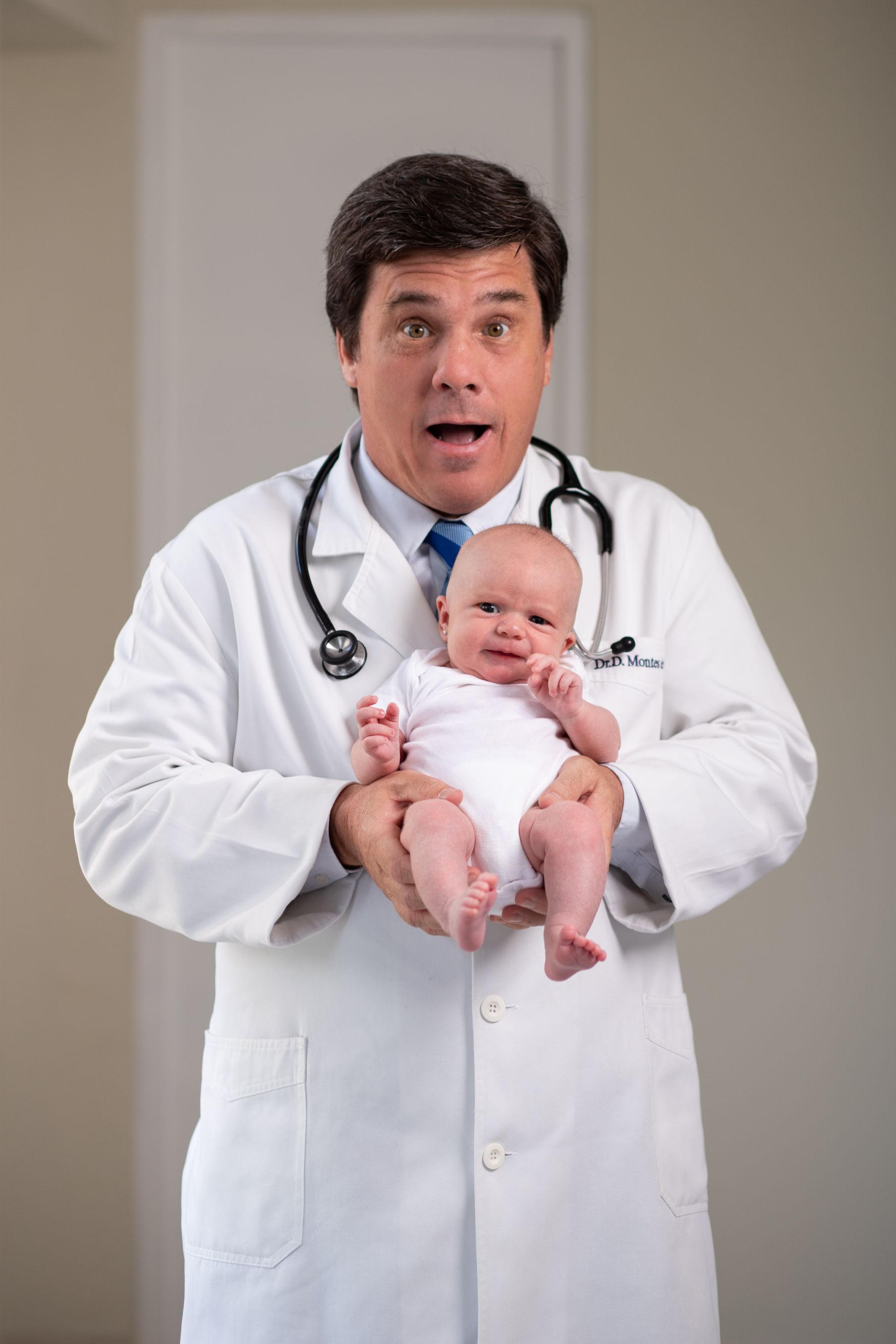 Un médico sostiene un bebé en sus brazos y pone cara de sorpresa.