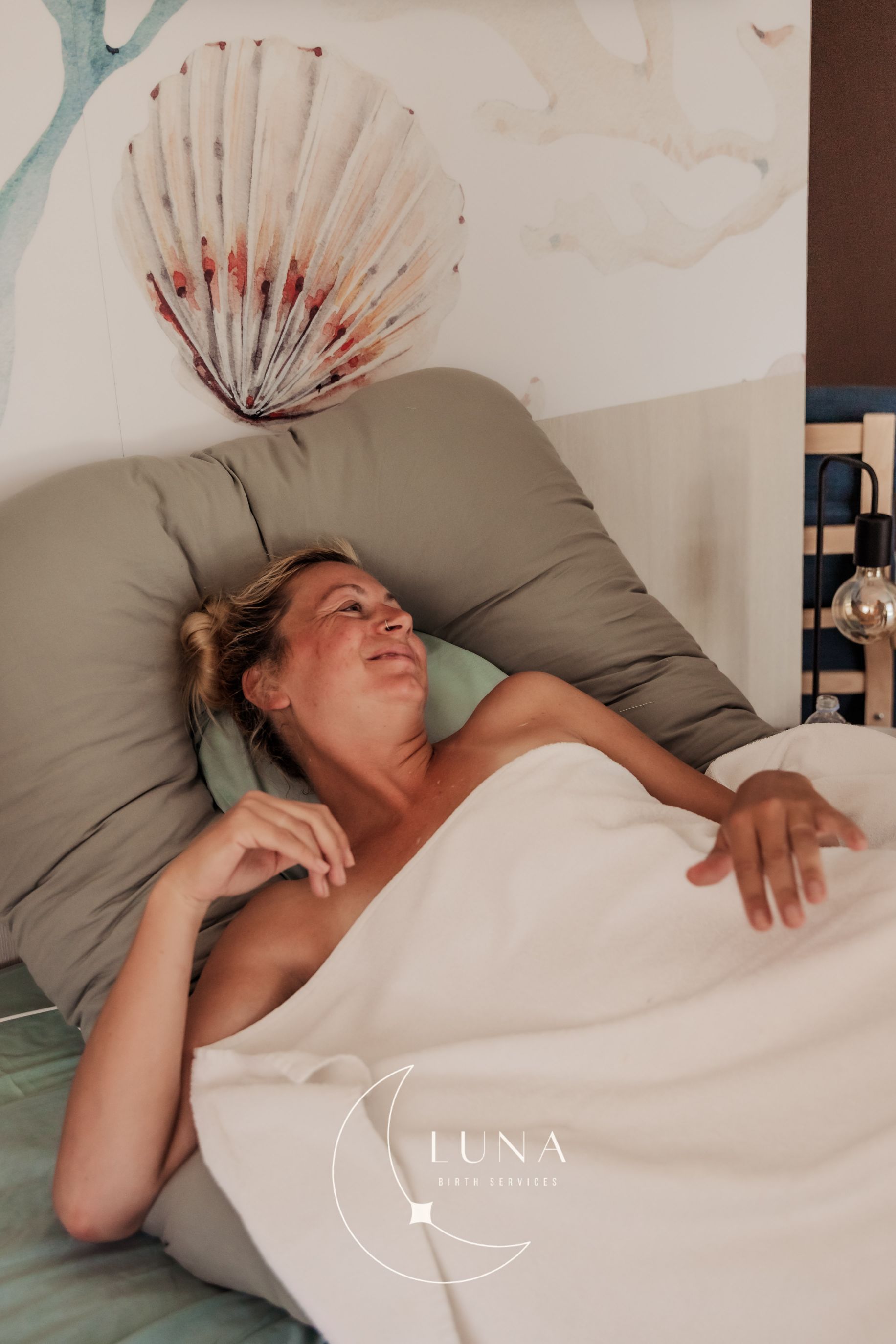 Una mujer está acostada en una cama con una manta blanca.